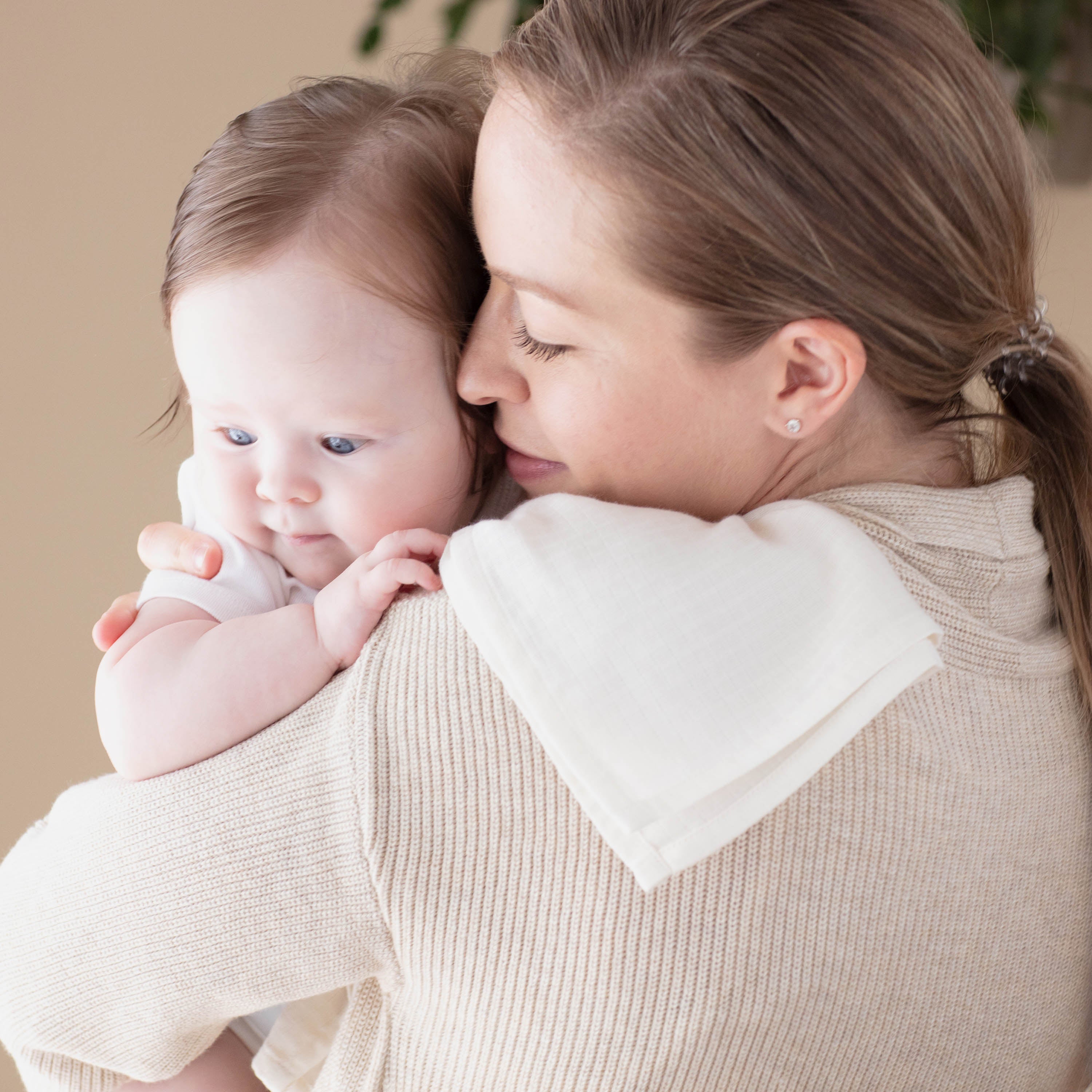 Woman holding a baby close together, both wearing light-colored clothing.