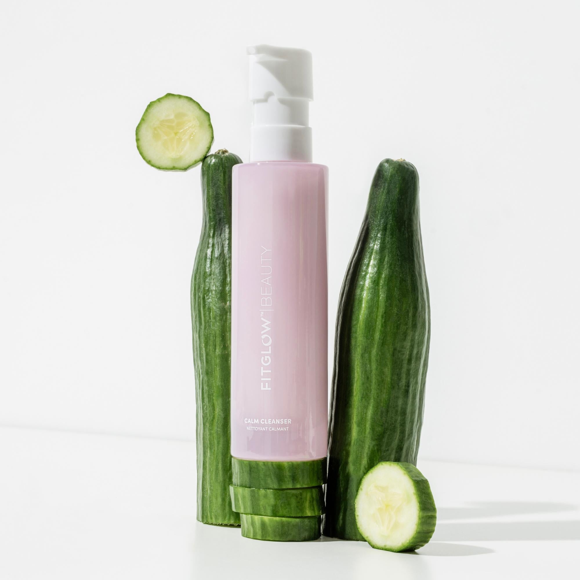 Pink skincare bottle with cucumbers on a white background