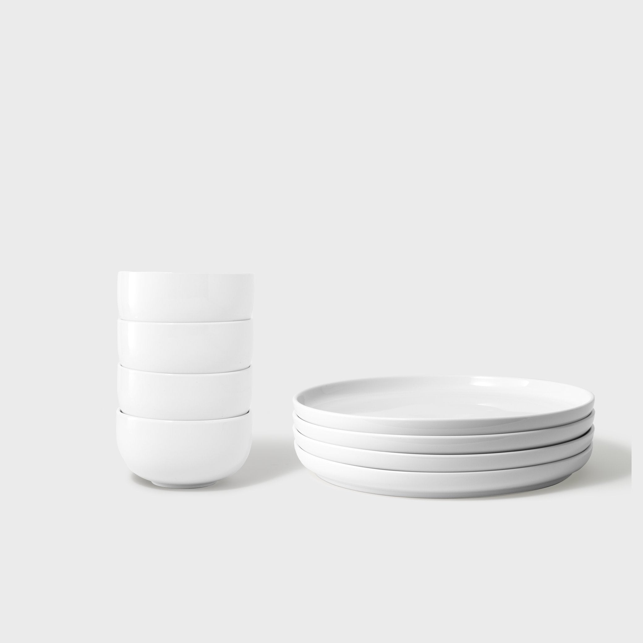 Set of white ceramic bowls and a glass on a light gray background