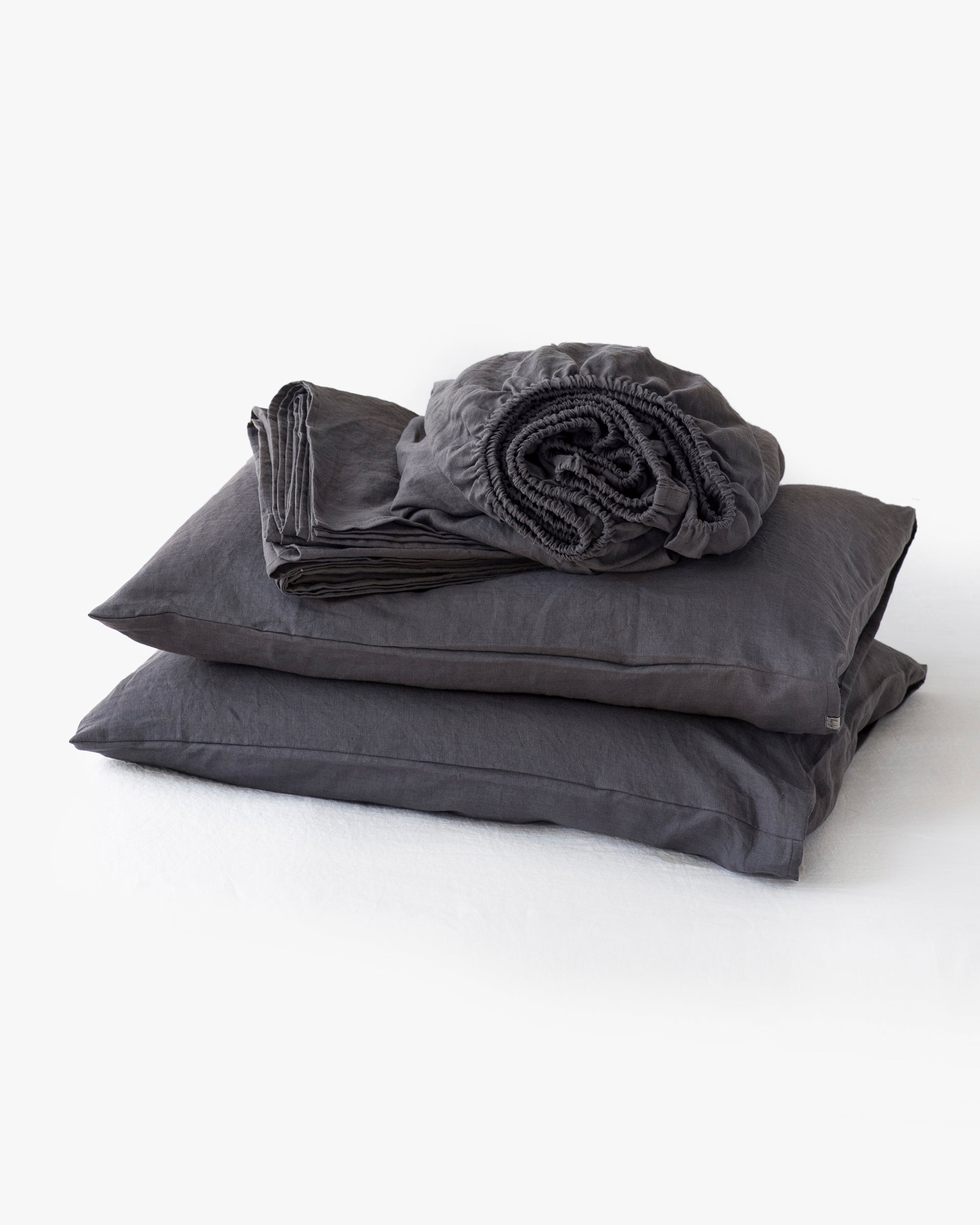 Set of dark gray bedding including a fitted sheet, two pillows, and a duvet cover on a white background.