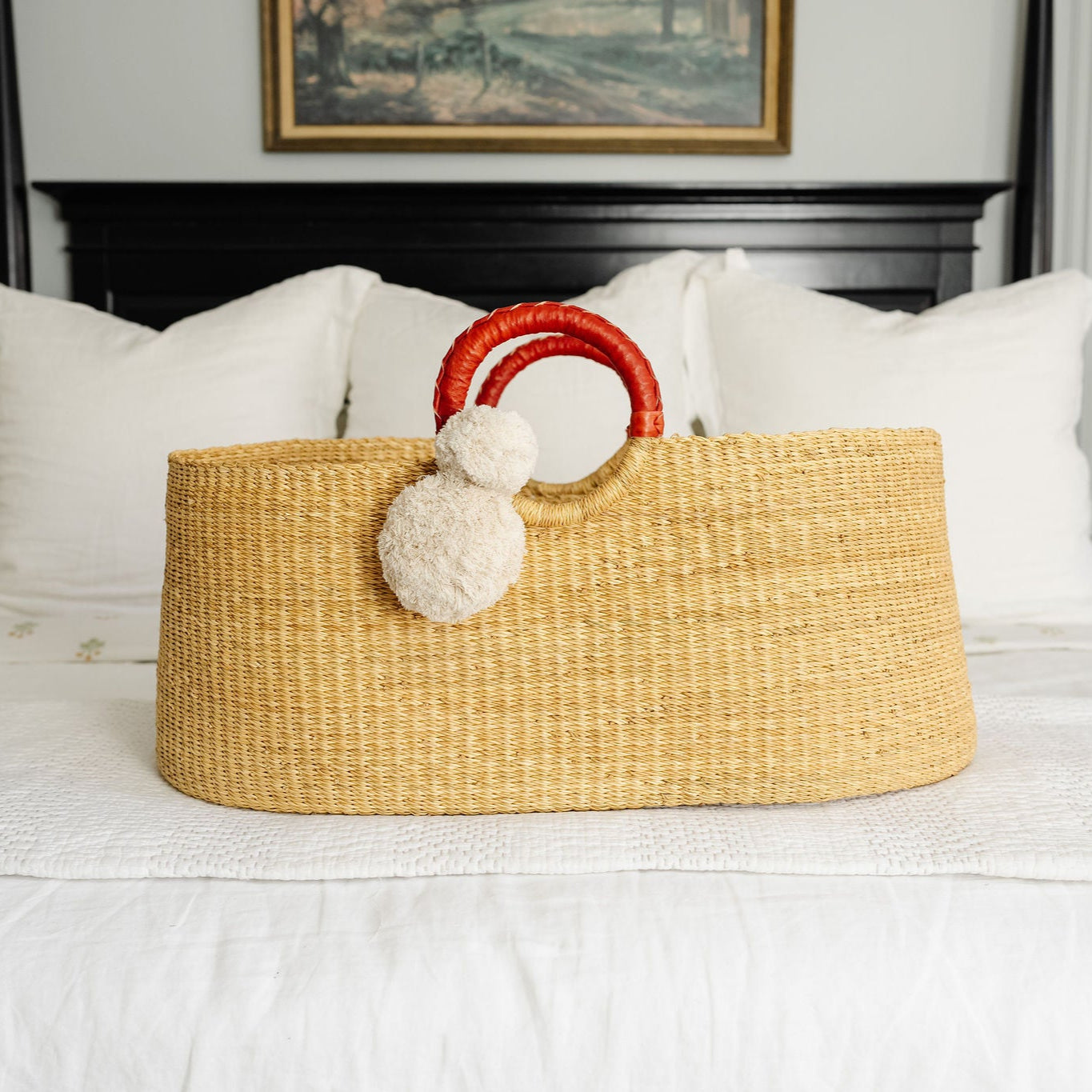 Woven basket with red handle and white pom-poms on a bed