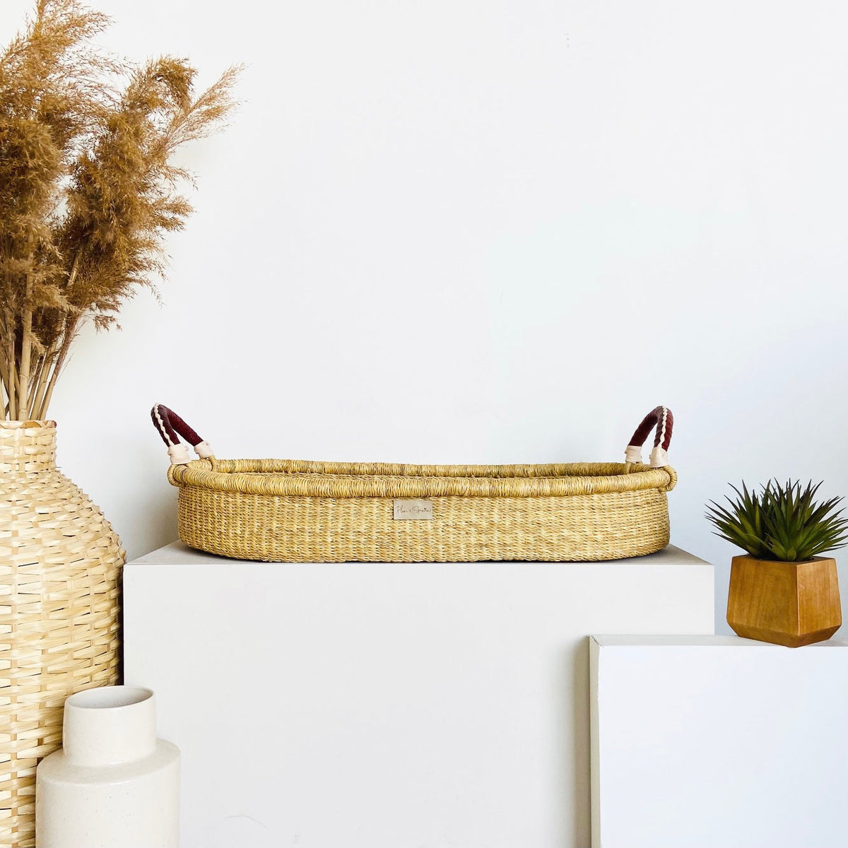 Wicker basket with handles on a white surface, surrounded by decorative items.