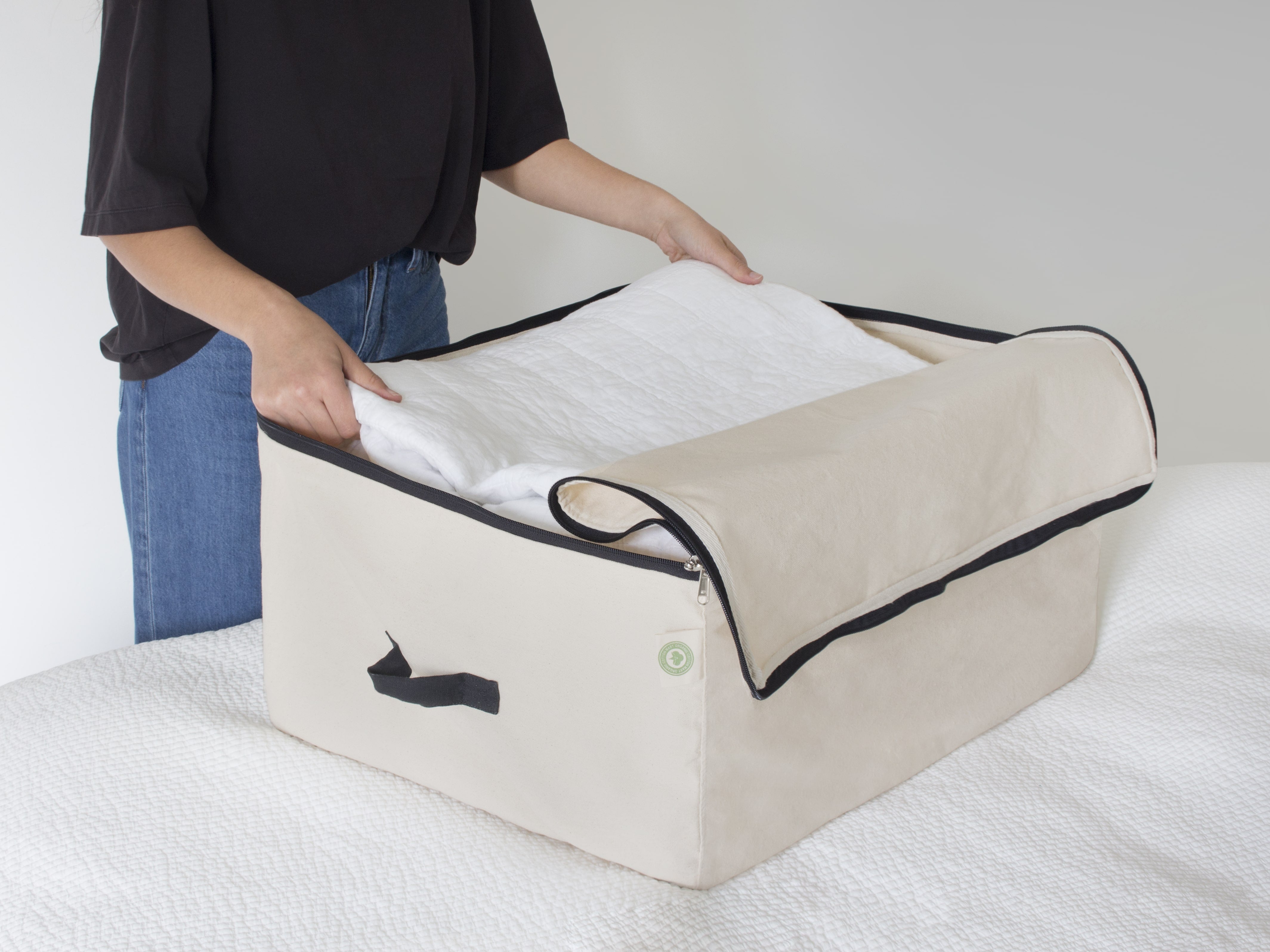 Person using a beige storage bag with a black zipper on a white surface