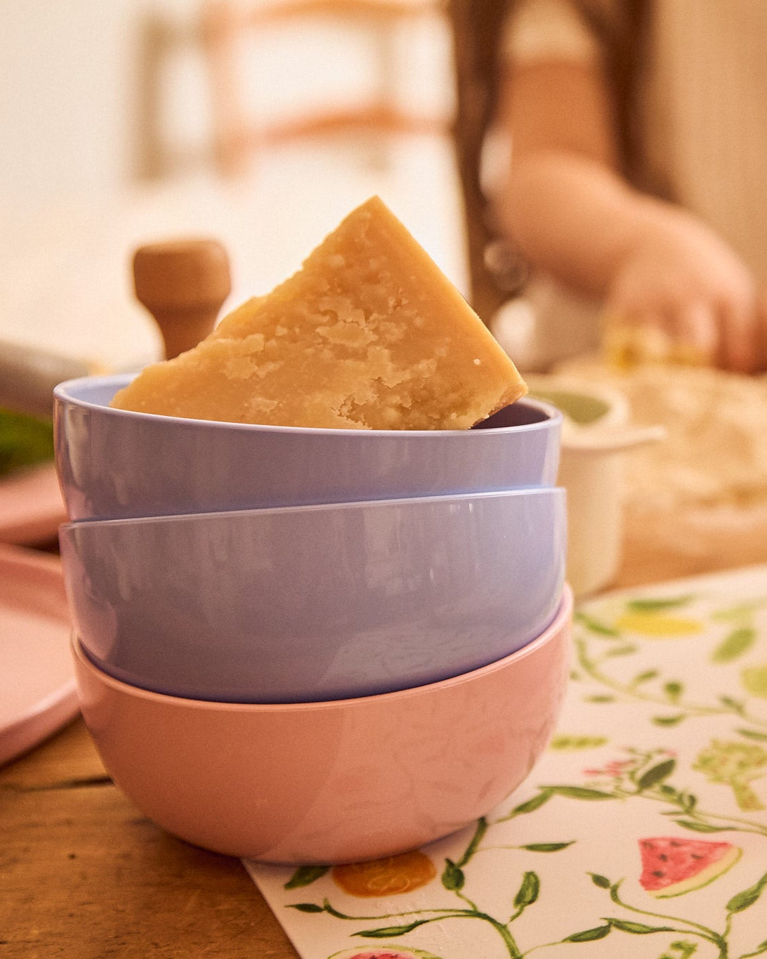 Stack of colorful bowls with a triangular piece of cheese on a floral tablecloth.