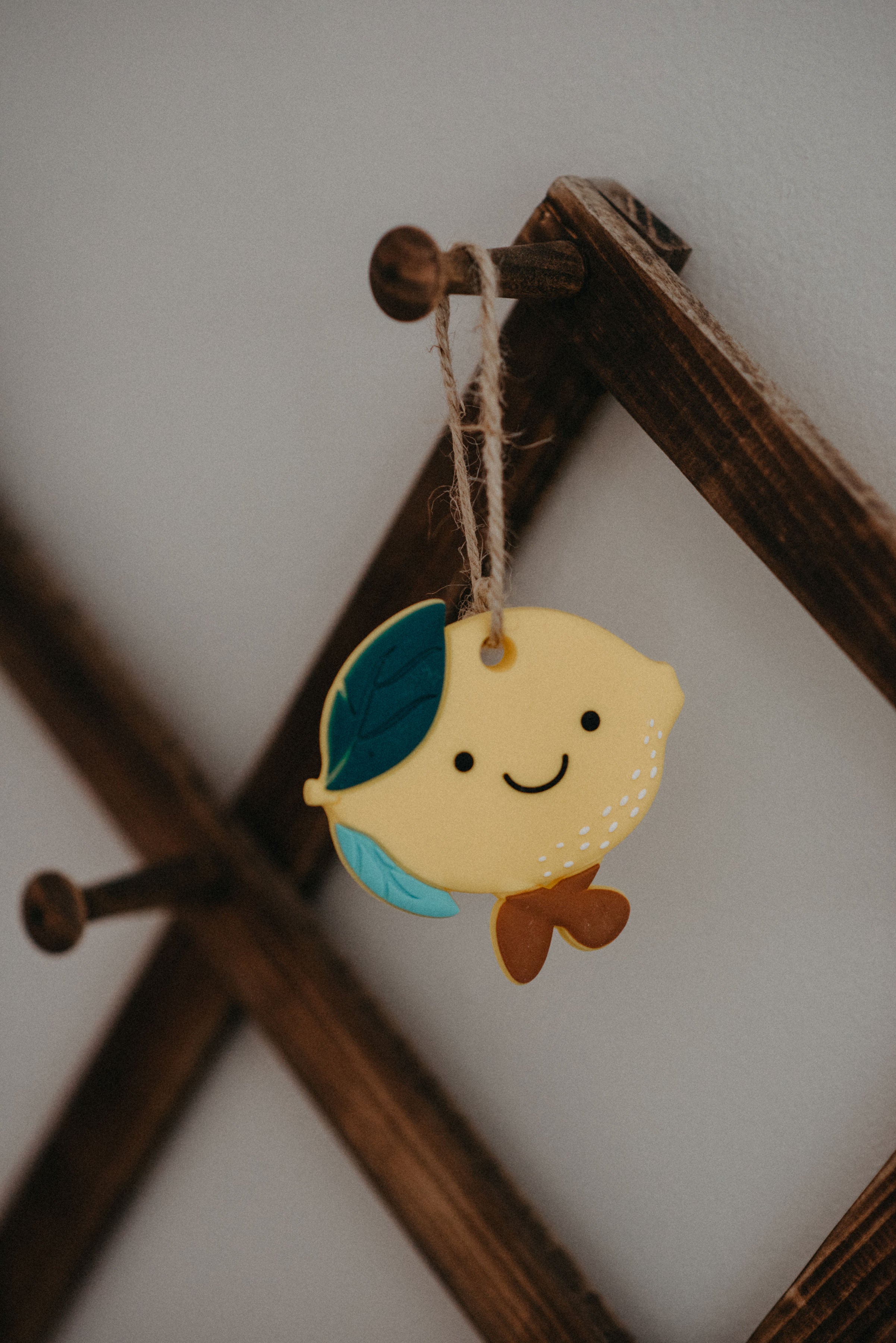 Decorative lemon-shaped ornament with a leaf hanging on a wooden hook.