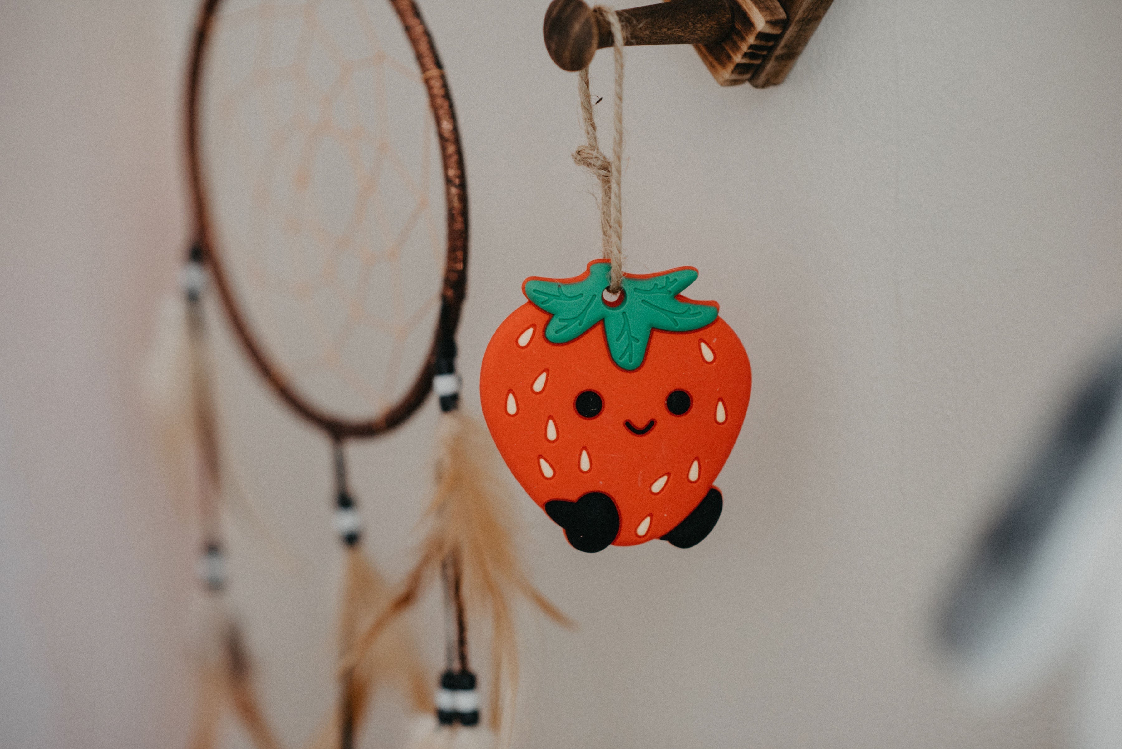 Decorative strawberry charm hanging from a dreamcatcher against a neutral background