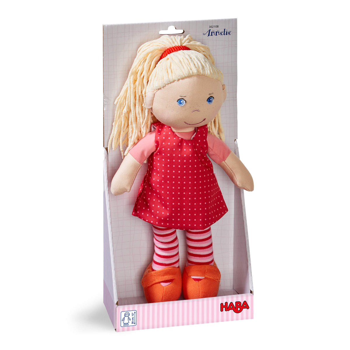 Doll in a red dress with white polka dots and striped leggings in a HABA box on a white background