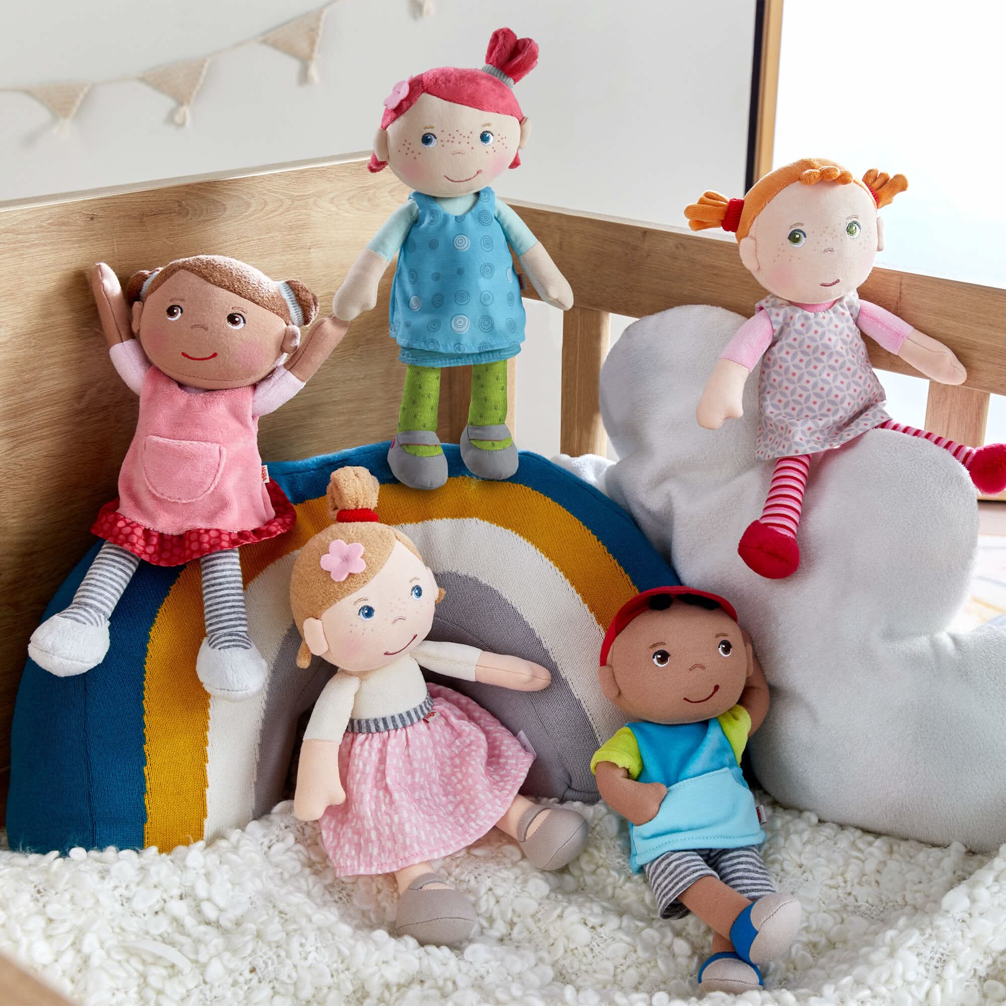 Set of plush dolls on a bed with a rainbow and cloud decoration.