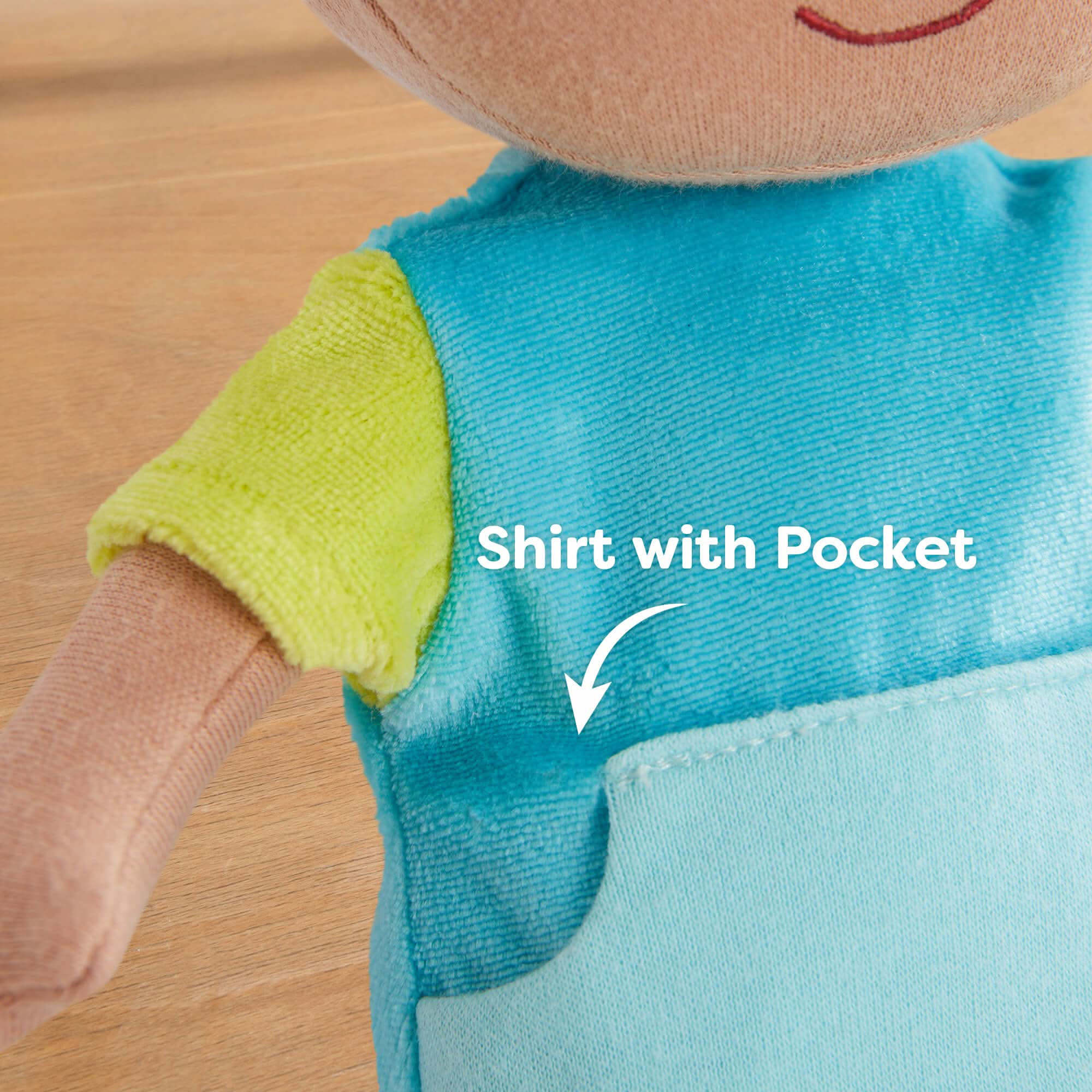Close-up of a plush toy wearing a blue shirt with a pocket on a wooden surface.