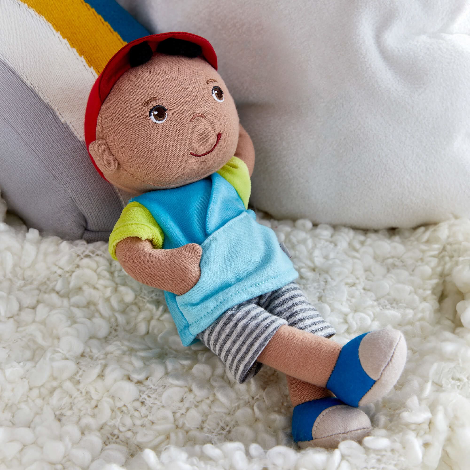 Toy figure of a child wearing a blue shirt, striped shorts, and a red cap on a white surface.