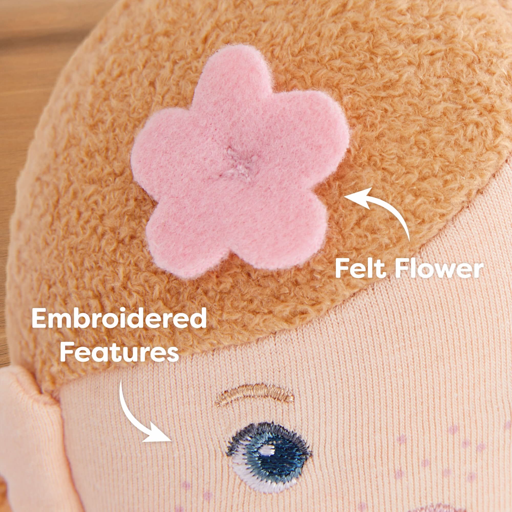 Close-up of a plush toy with embroidered features and a felt flower on a wooden surface.