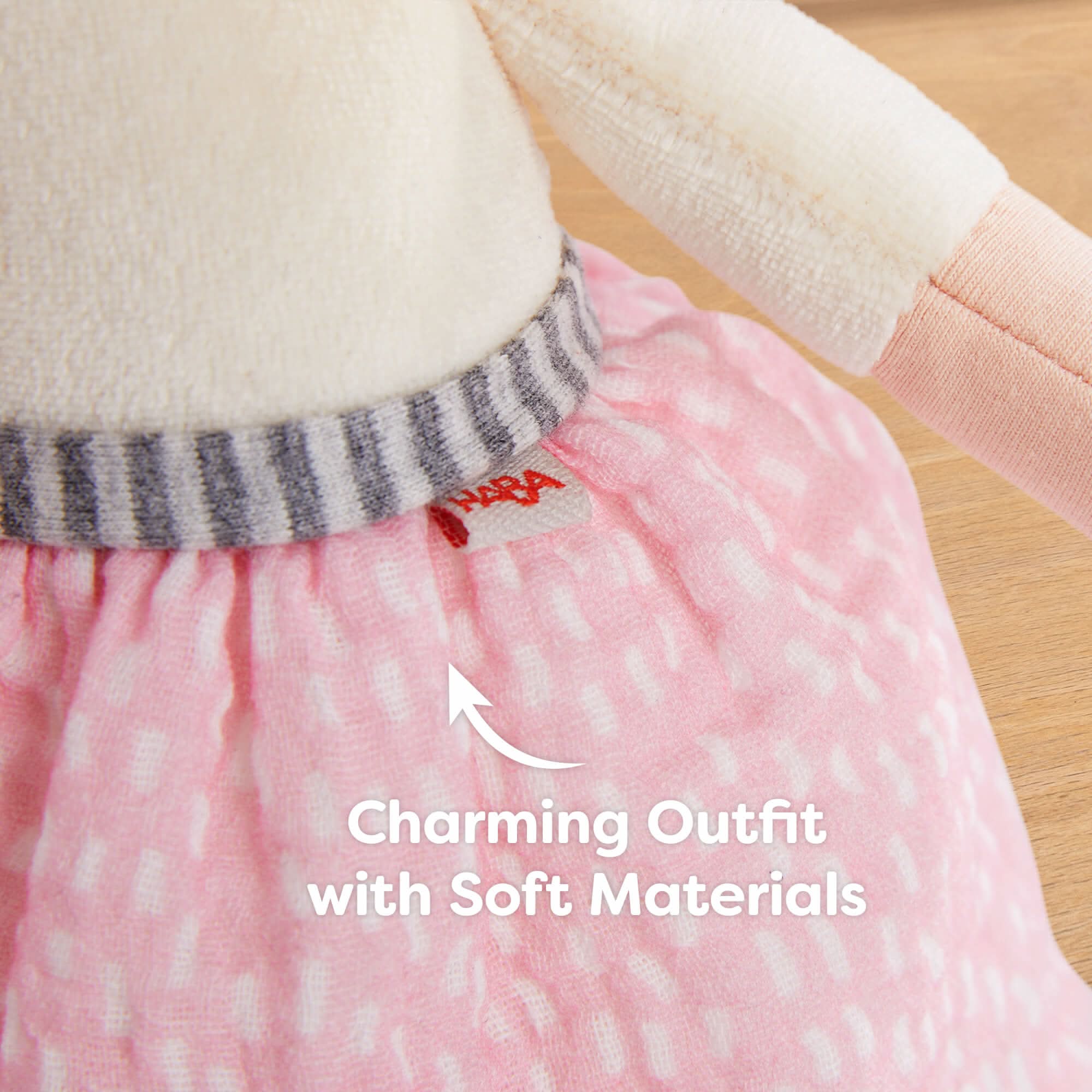 Close-up of a doll wearing a pink outfit with soft materials, featuring a brand label.