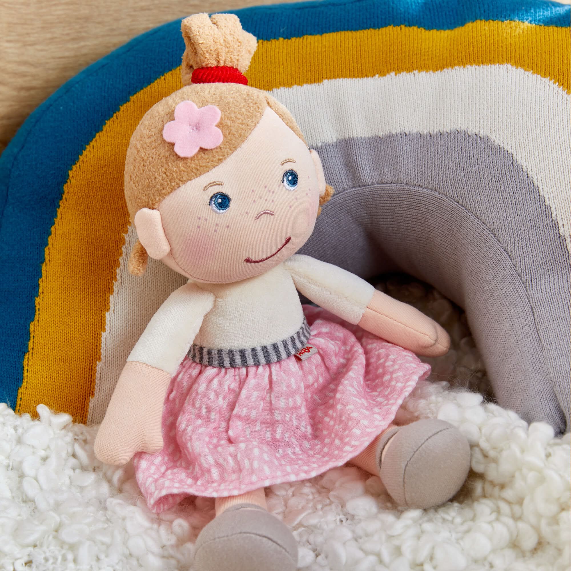 Plush toy doll with a pink dress and flower headband on a colorful background
