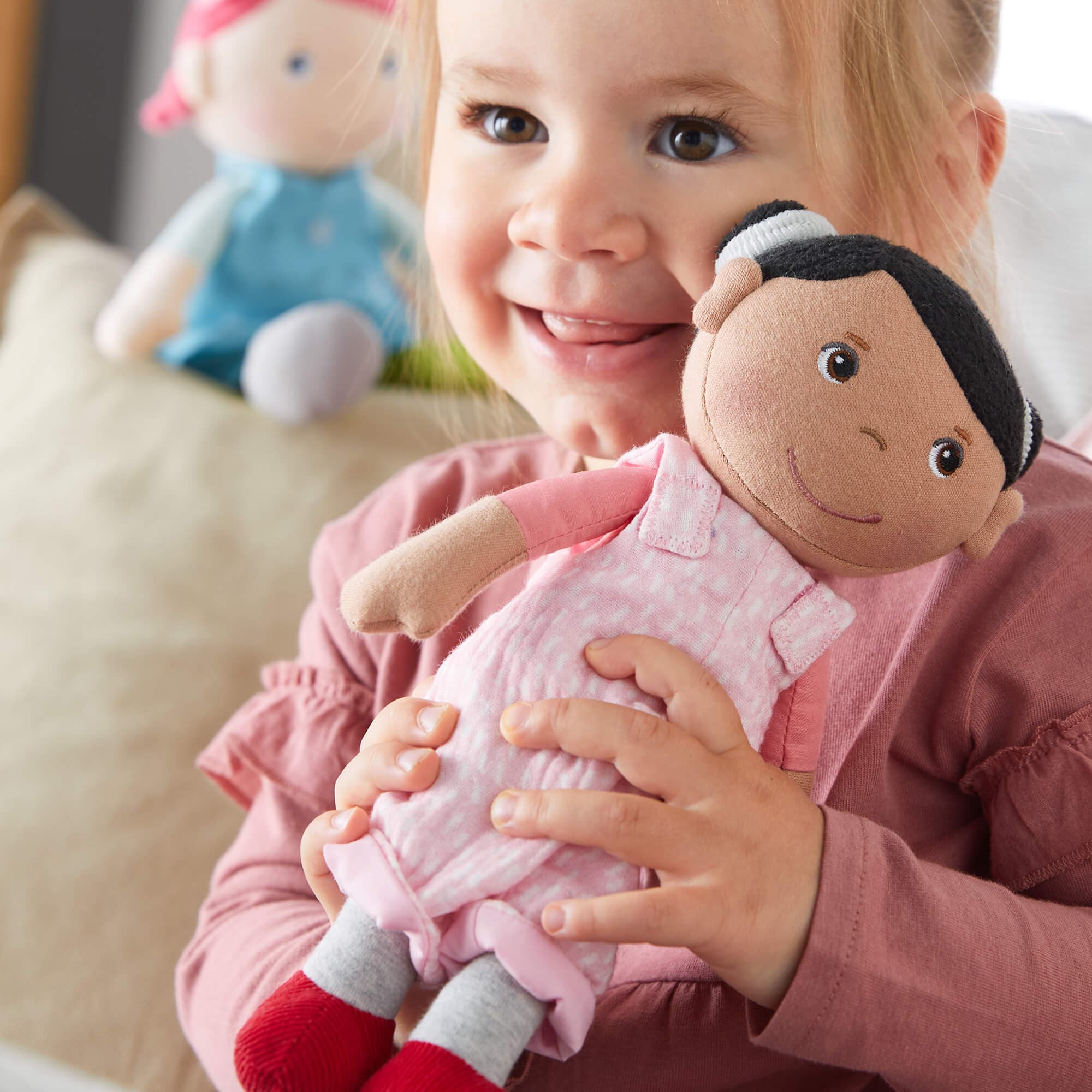 Child holding a plush doll with another doll in the background
