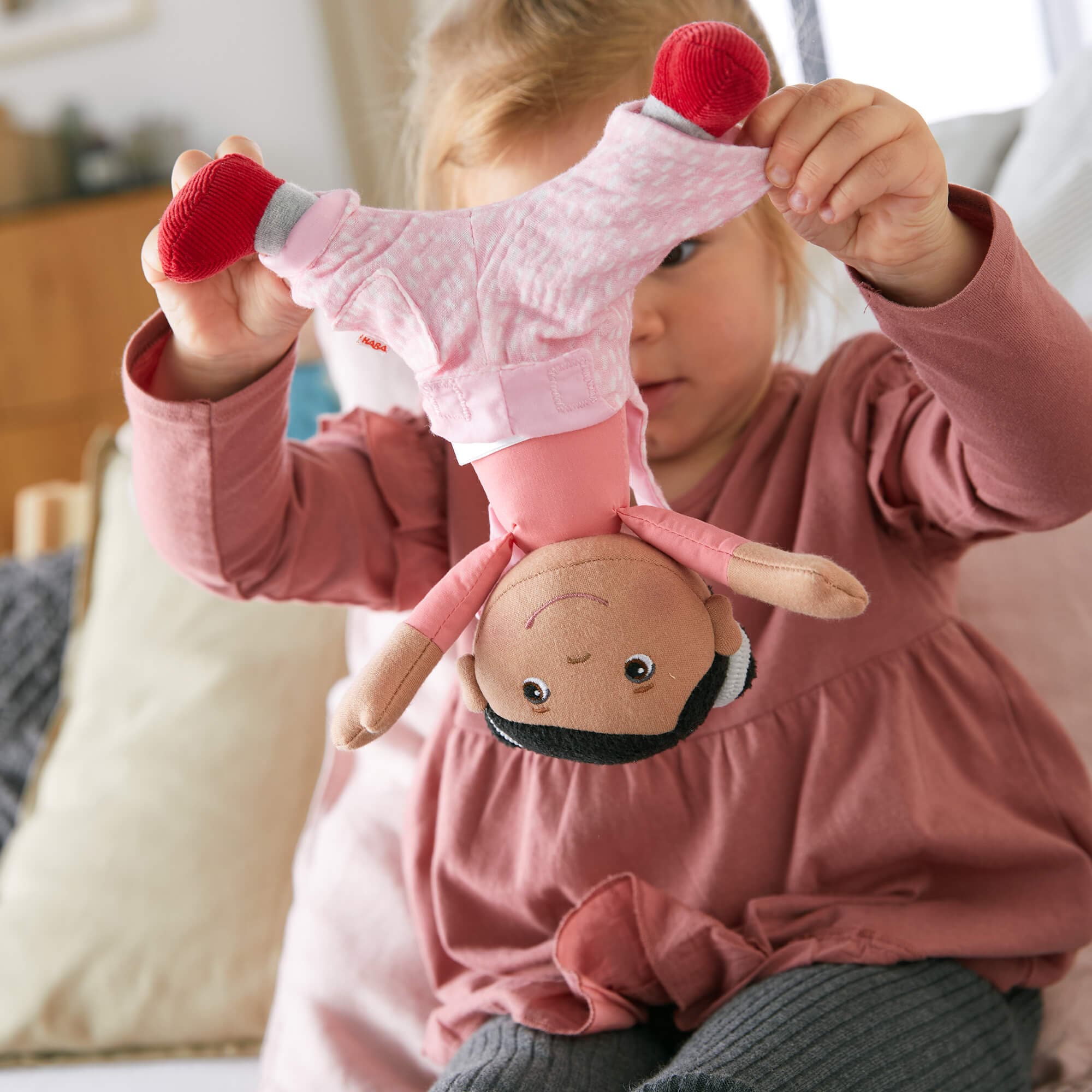 Child holding a plush toy with a face and red pom-poms.