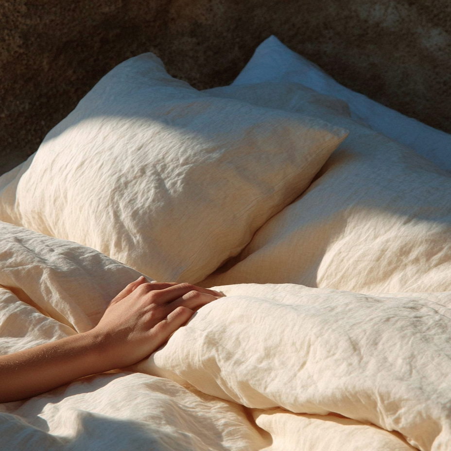 Close-up of a person's hand resting on soft beige bedding with pillows.