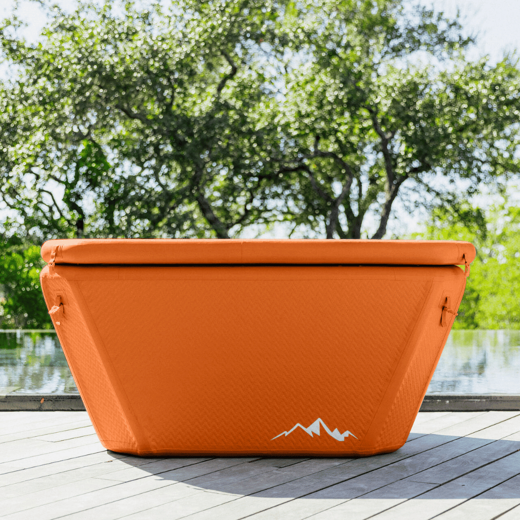 Orange cooler bag with a mountain logo on a wooden deck with greenery in the background