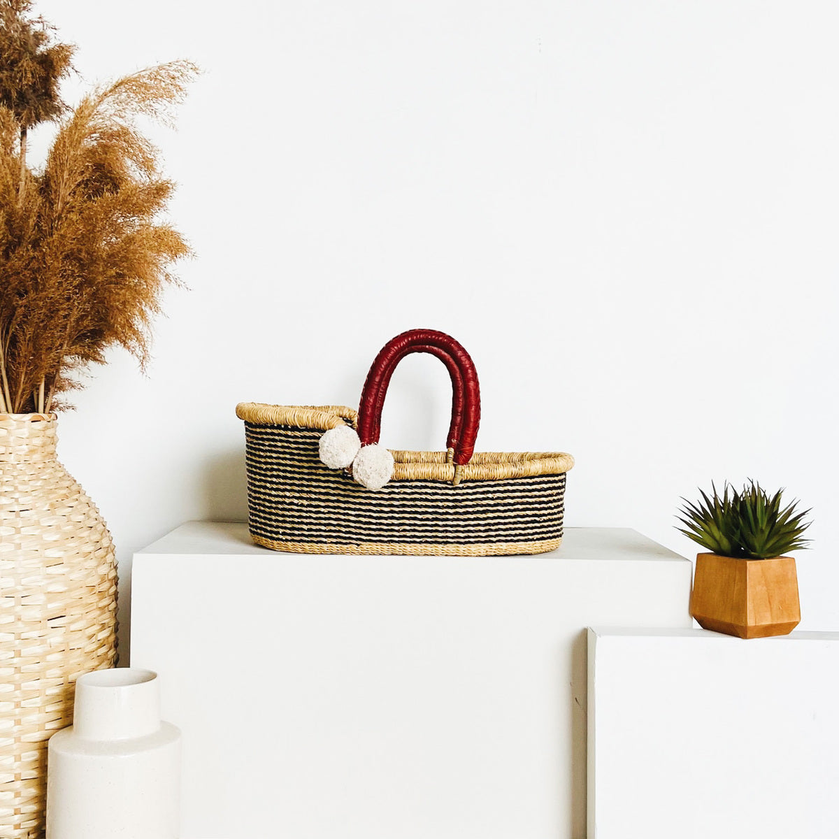 Woven basket with red handle on a white surface with decorative items.