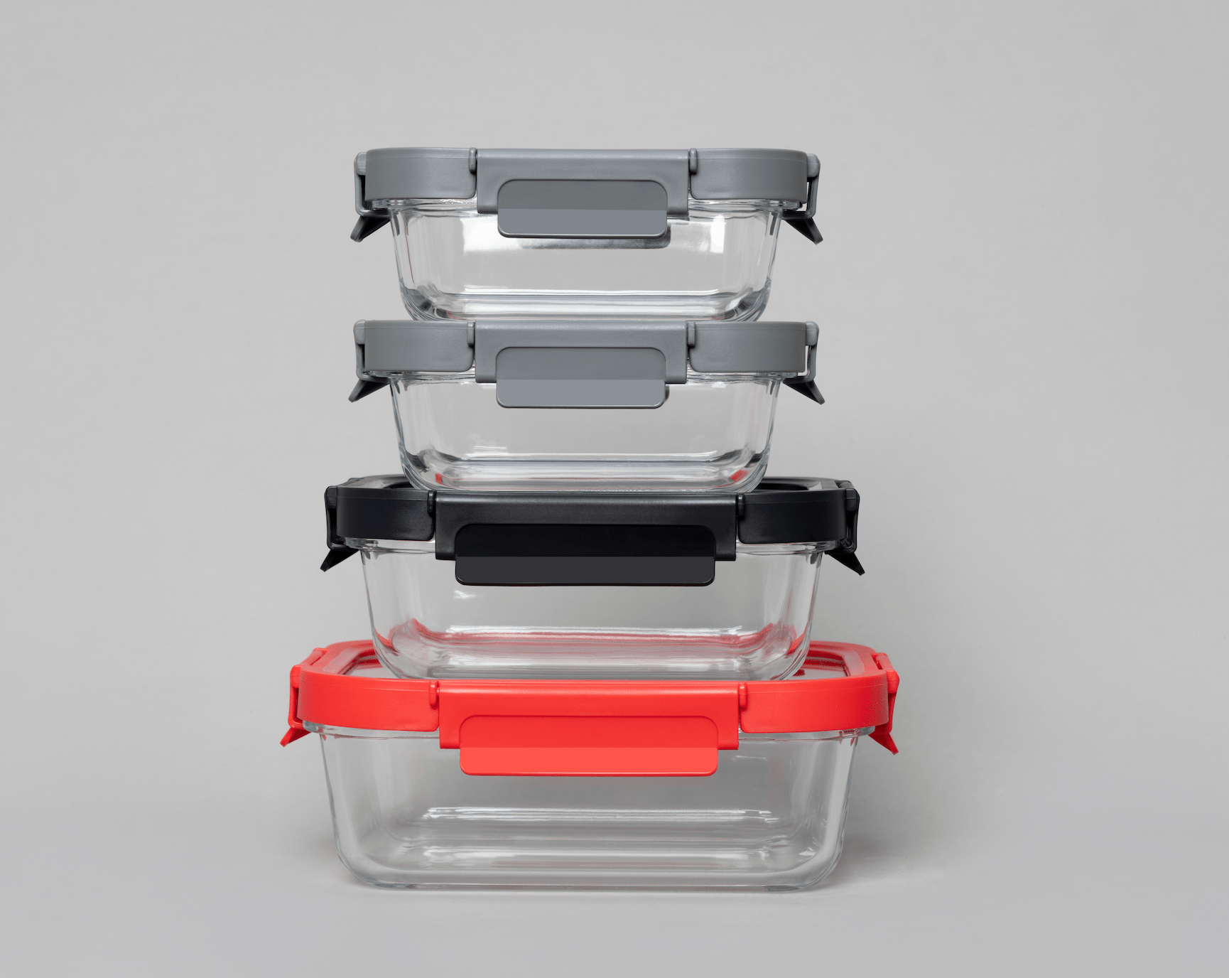 Stack of clear glass food containers with various colored lids on a gray background