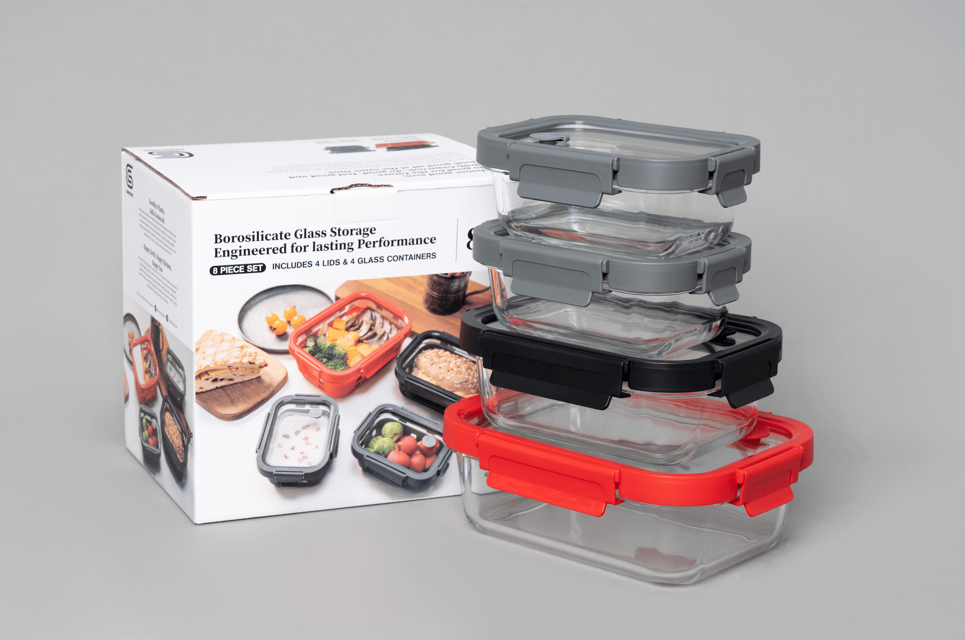 Set of glass food storage containers with red and black lids next to their packaging on a gray background