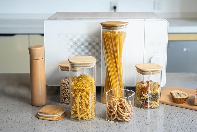 Glass jars with wooden lids containing various dry foods on a kitchen counter.