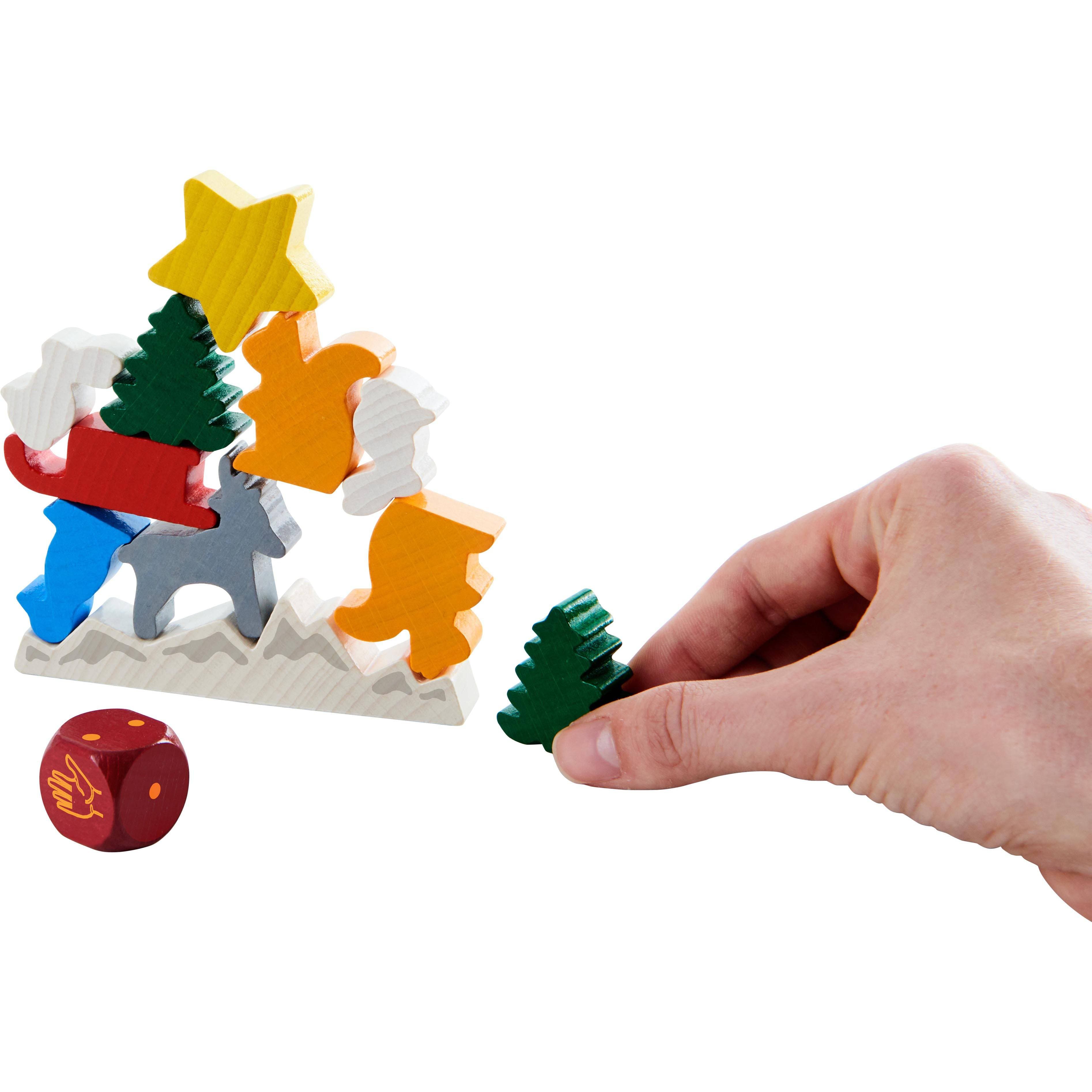 Colorful wooden toy with figures and a hand placing a green tree piece on a white background