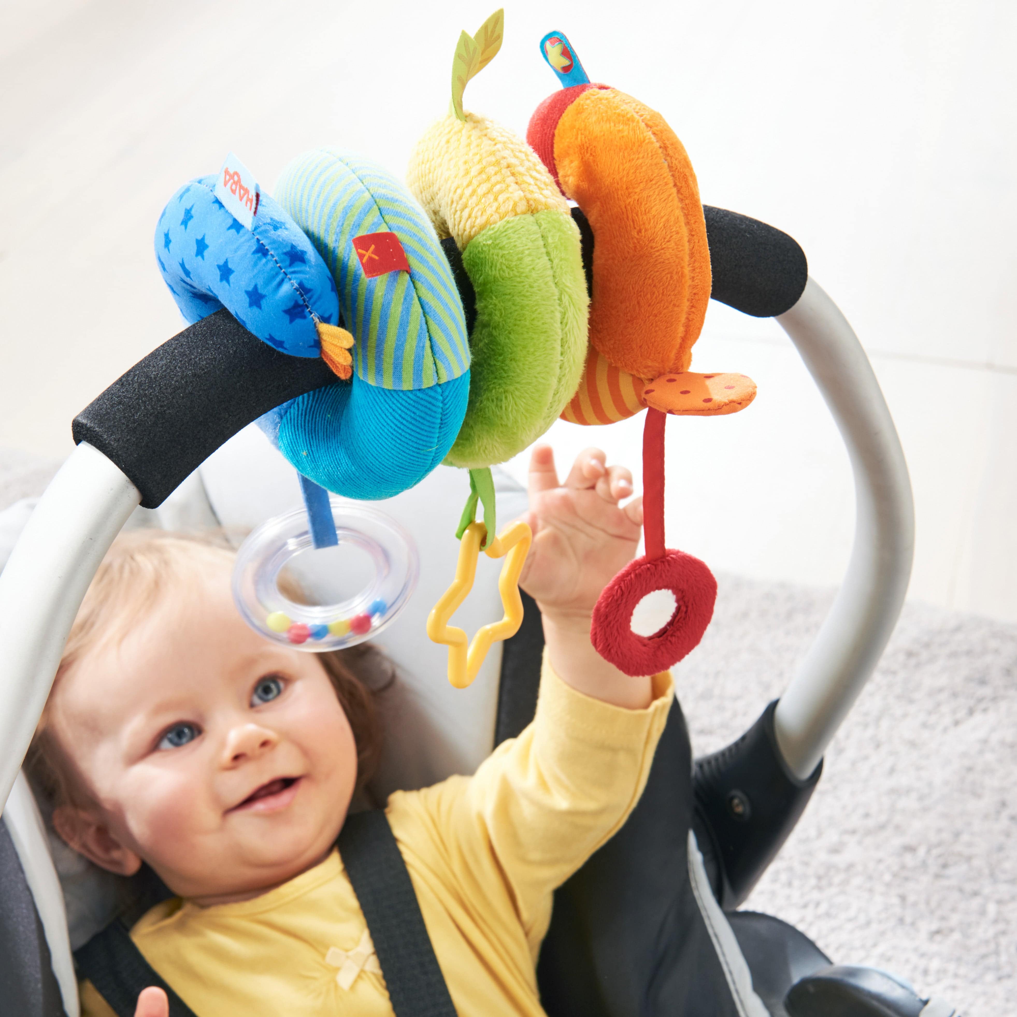 Baby in a stroller with colorful toy hanging above