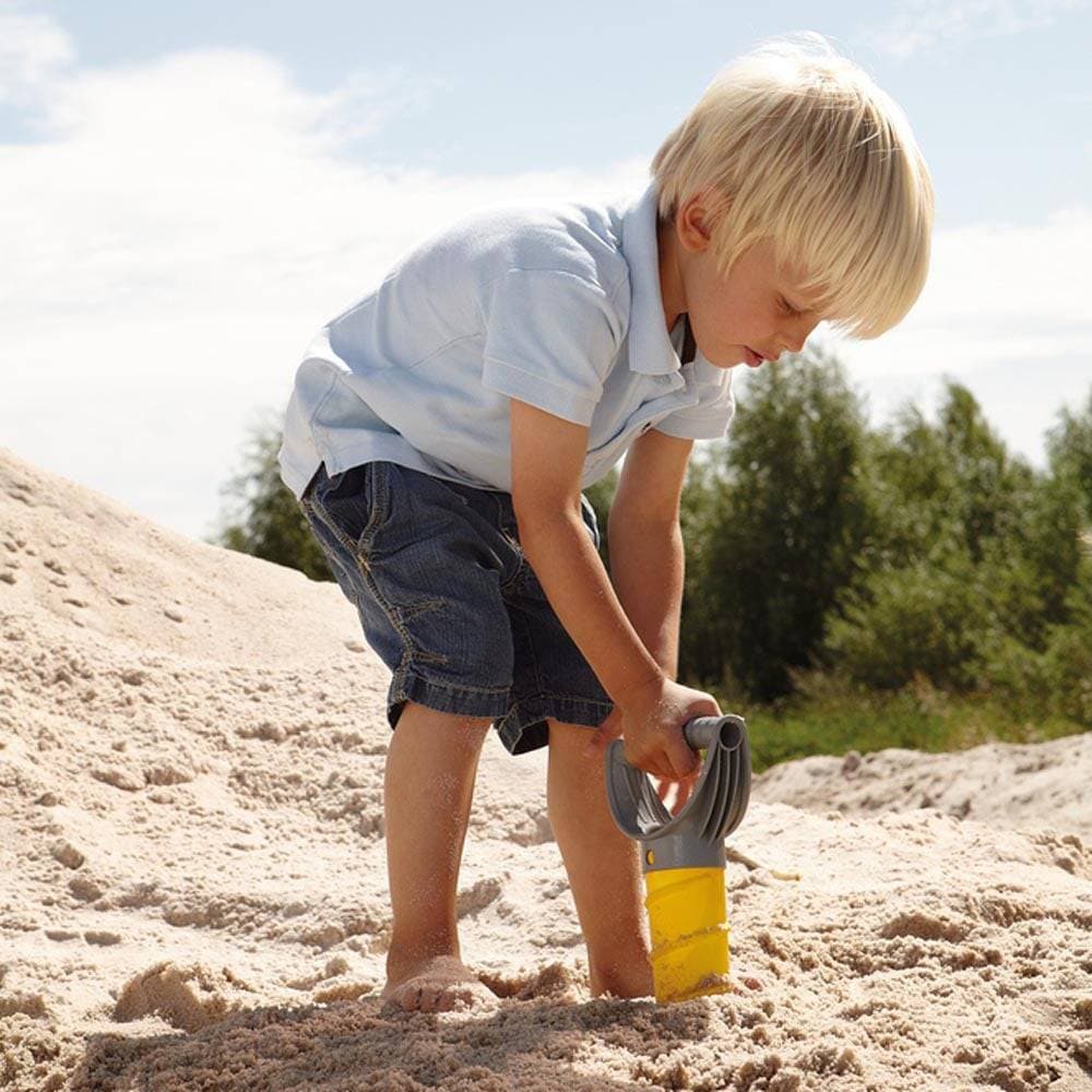 Child playing in sand with a yellow toy shovel on a sunny day