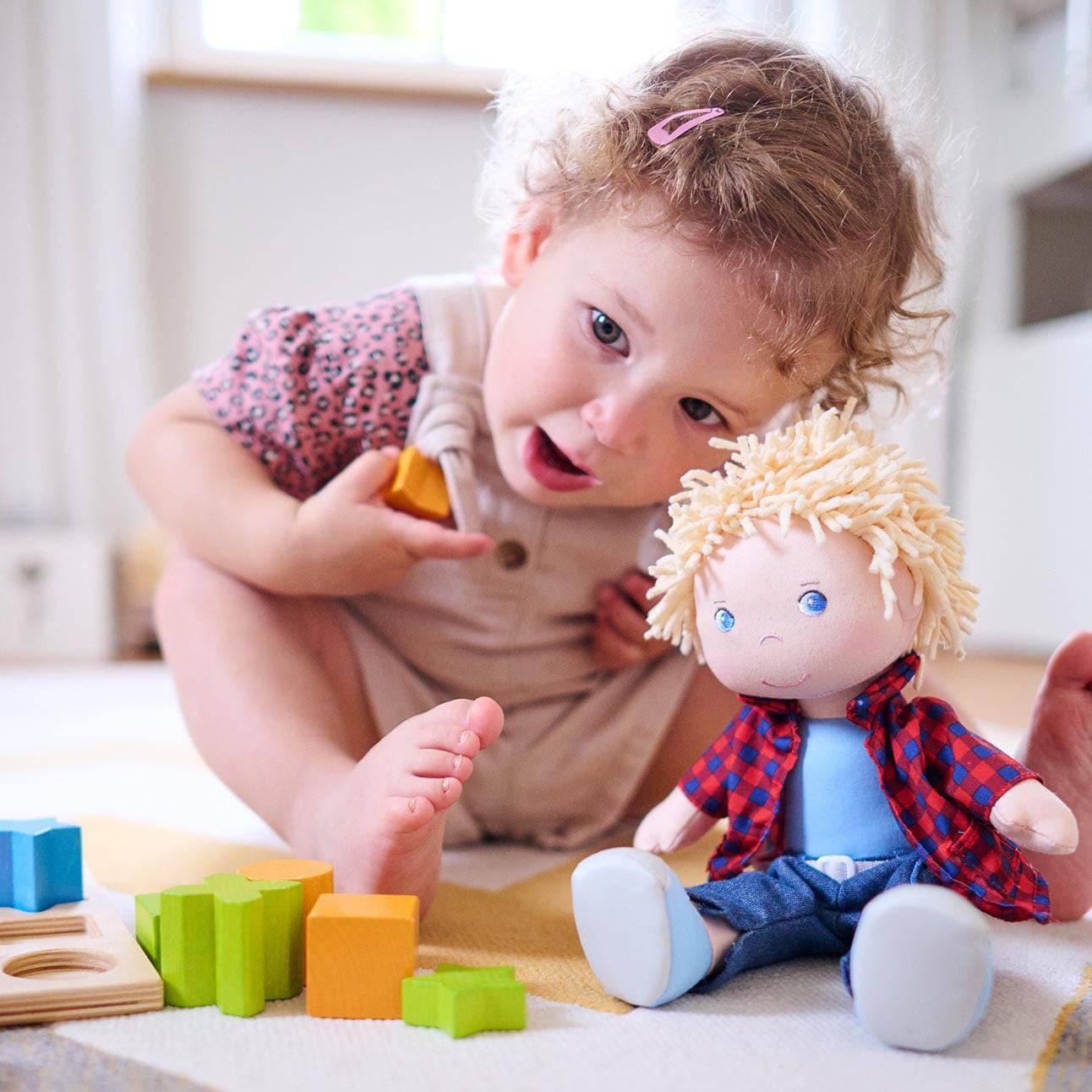 Child playing with toys and a doll on a light-colored floor.