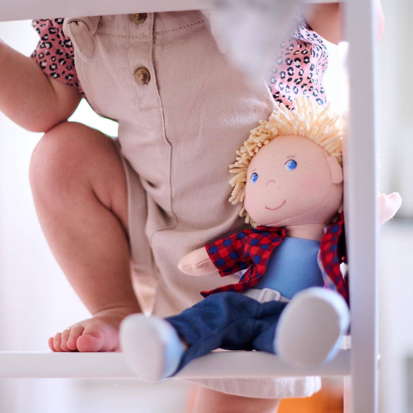 Child sitting on a step with a doll wearing a red and blue outfit.