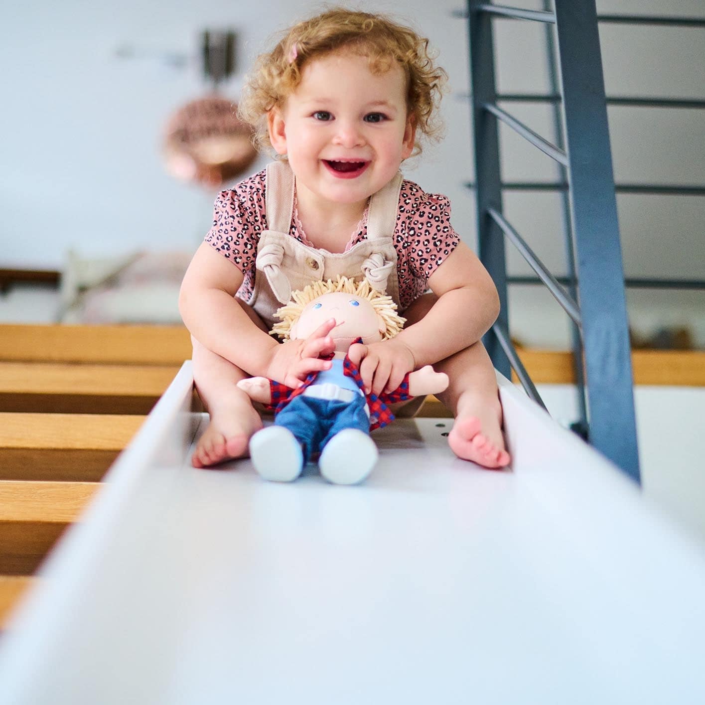 Child sitting on a slide holding a doll in a playroom.