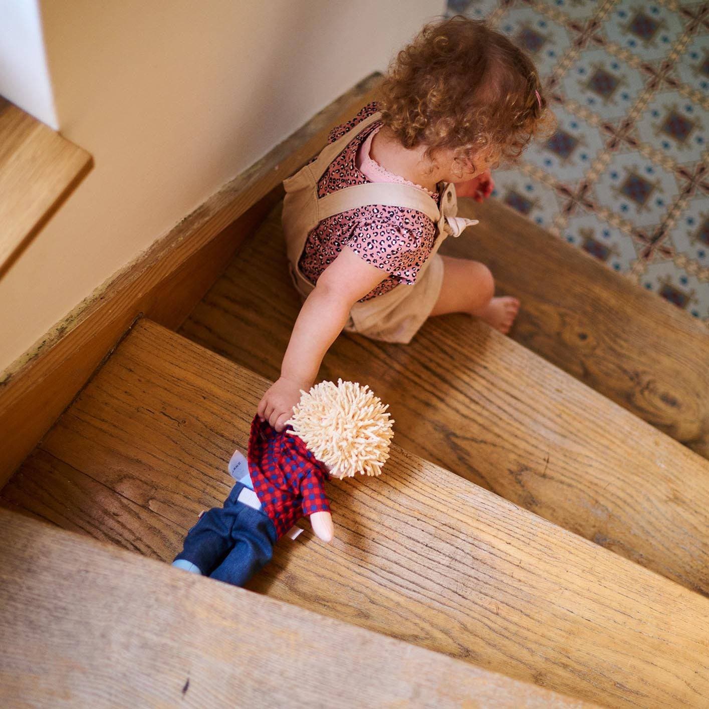 Child climbing wooden stairs holding a doll