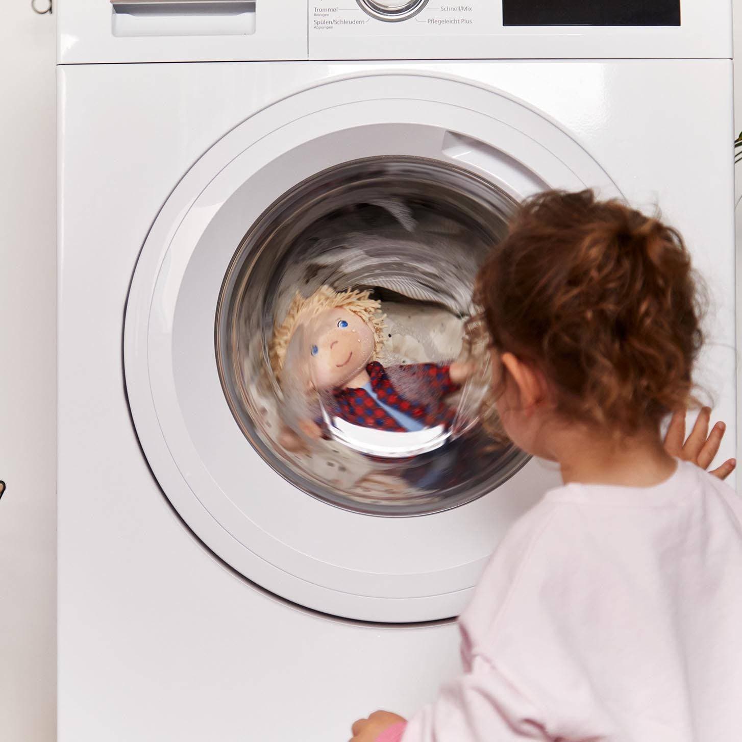 Child looking into a washing machine with a doll inside