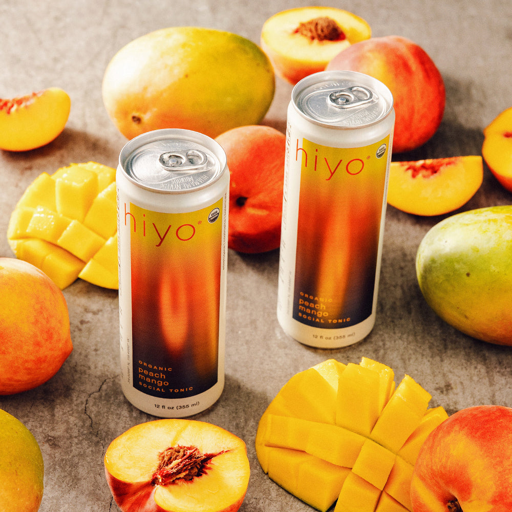 Two cans of 'Hiyo' fruit juice with peaches and mangoes on a stone surface