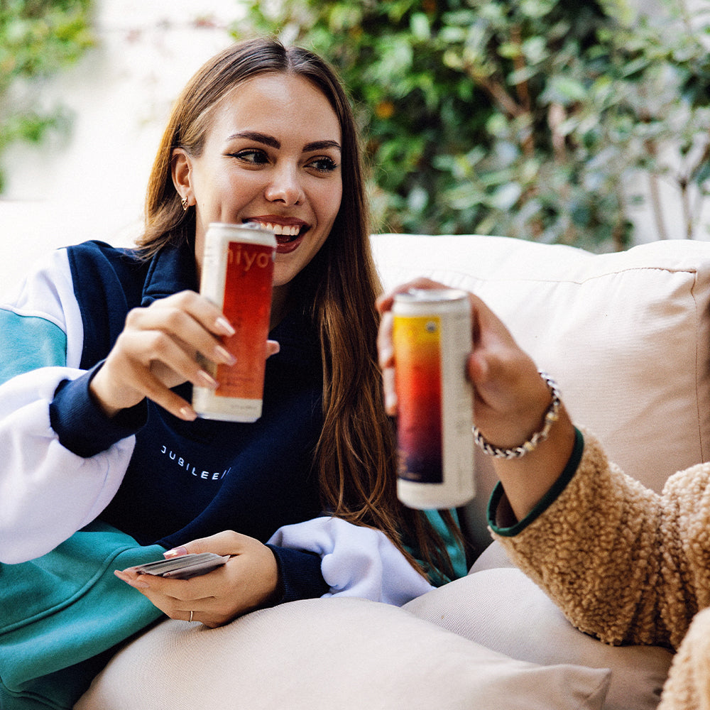 Two people sitting on a couch outdoors, holding drinks and smiling.