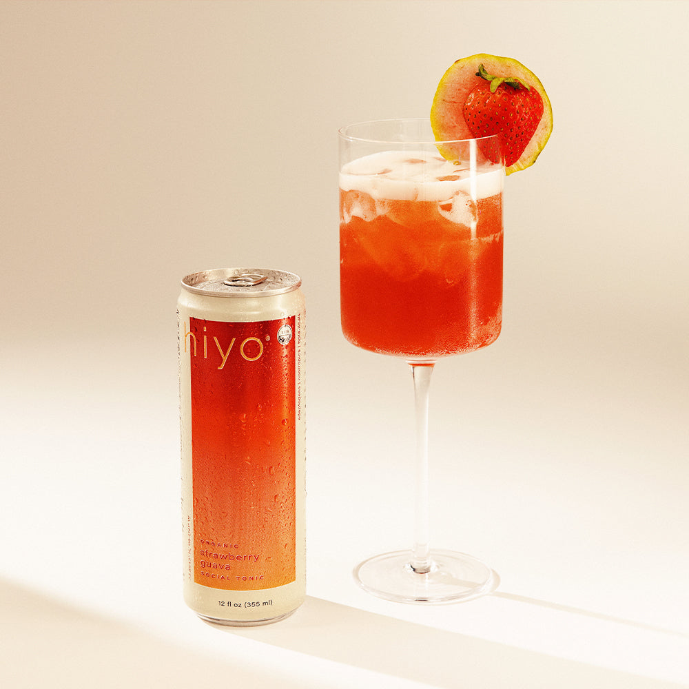 Red cocktail in a glass with a strawberry garnish next to a can labeled 'hiyo' on a light background