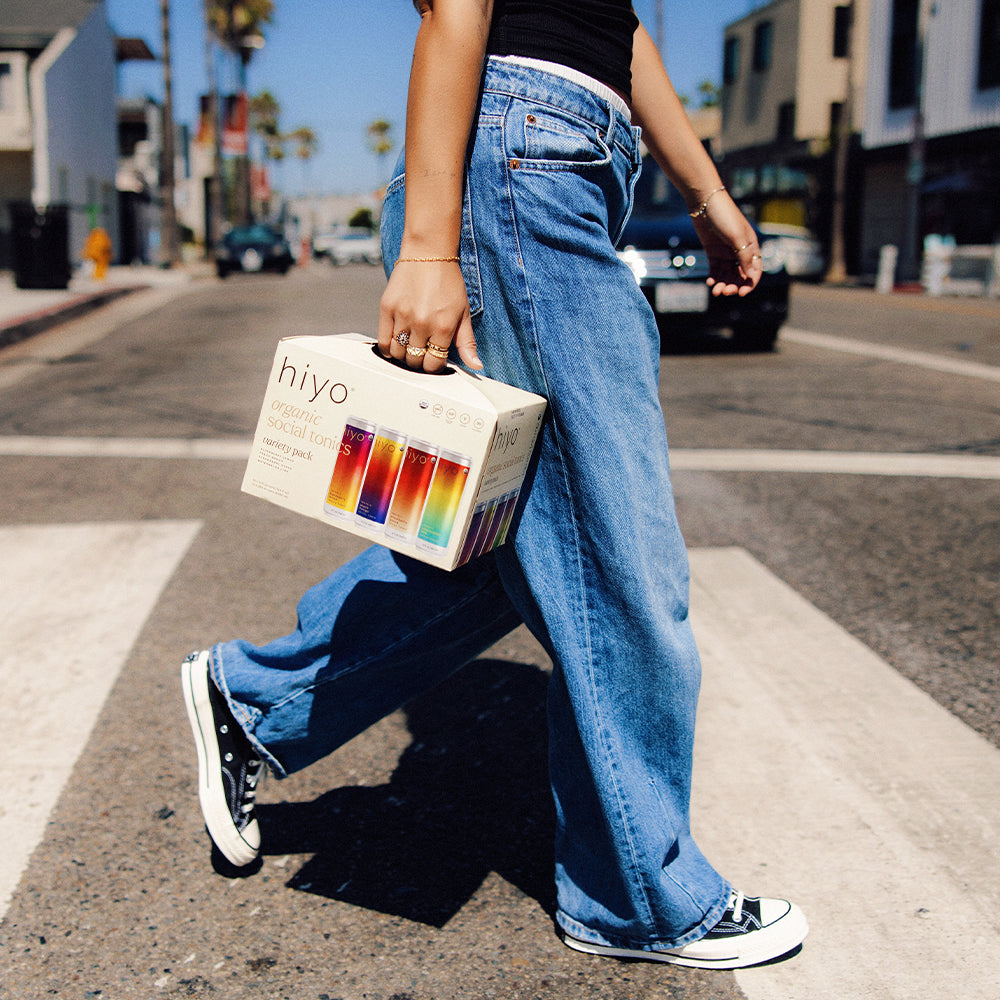 Person holding a 'hiyo' box with colorful drinks on a city street.