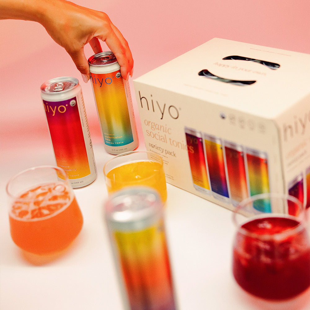 hiyo organic social tonic cans and glasses with a box on a pink background
