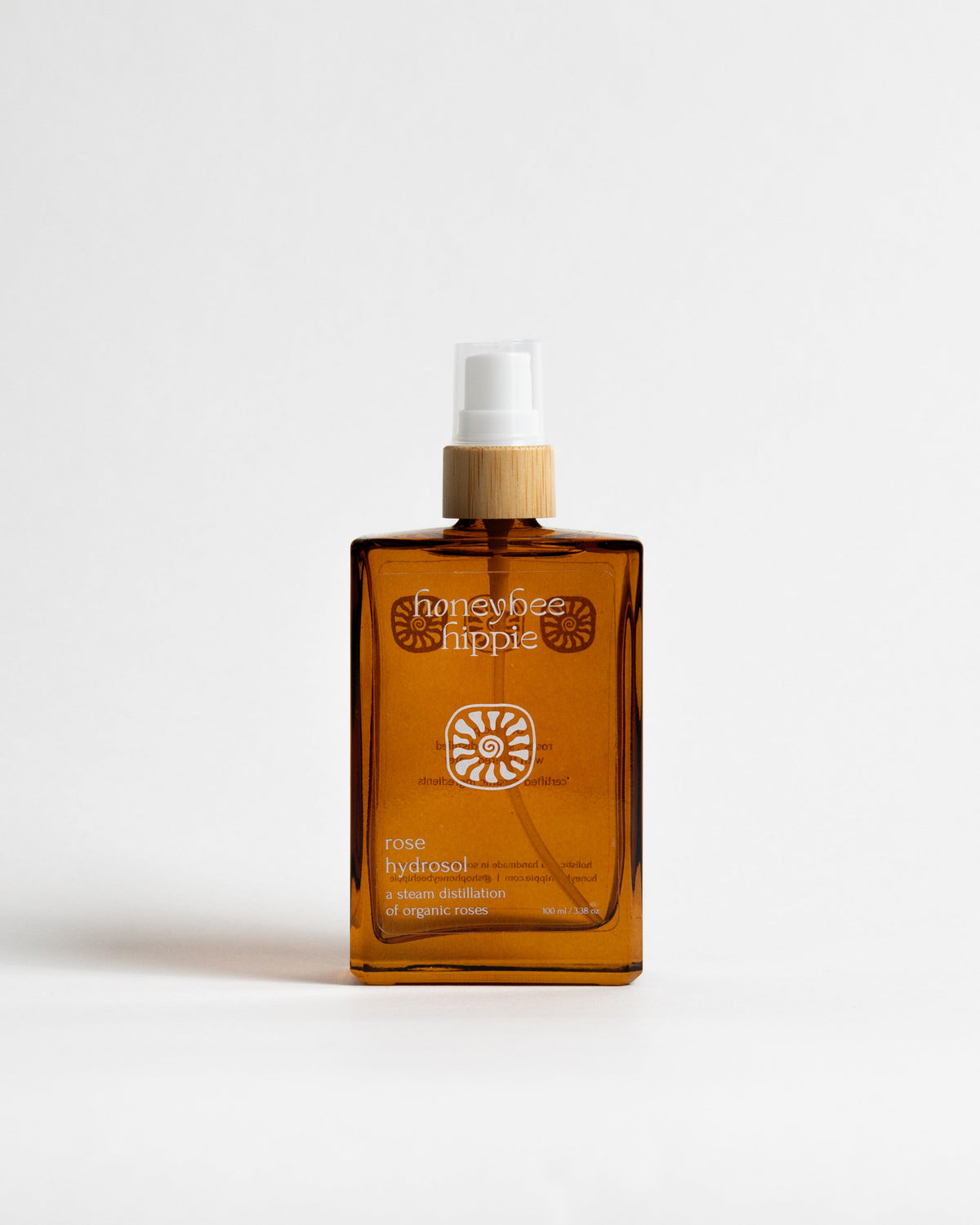 An amber glass spray bottle of Honeybee Hippie Note Hydrocol liquid steam distillation with a bamboo collar and white spray top, set against a plain white background.