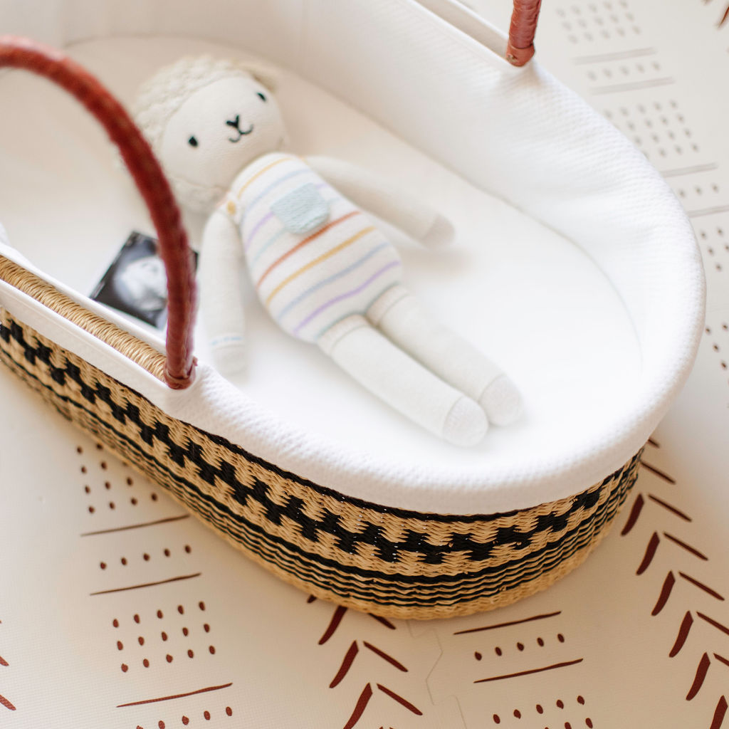 Baby doll in a bassinet with a striped blanket on a patterned surface