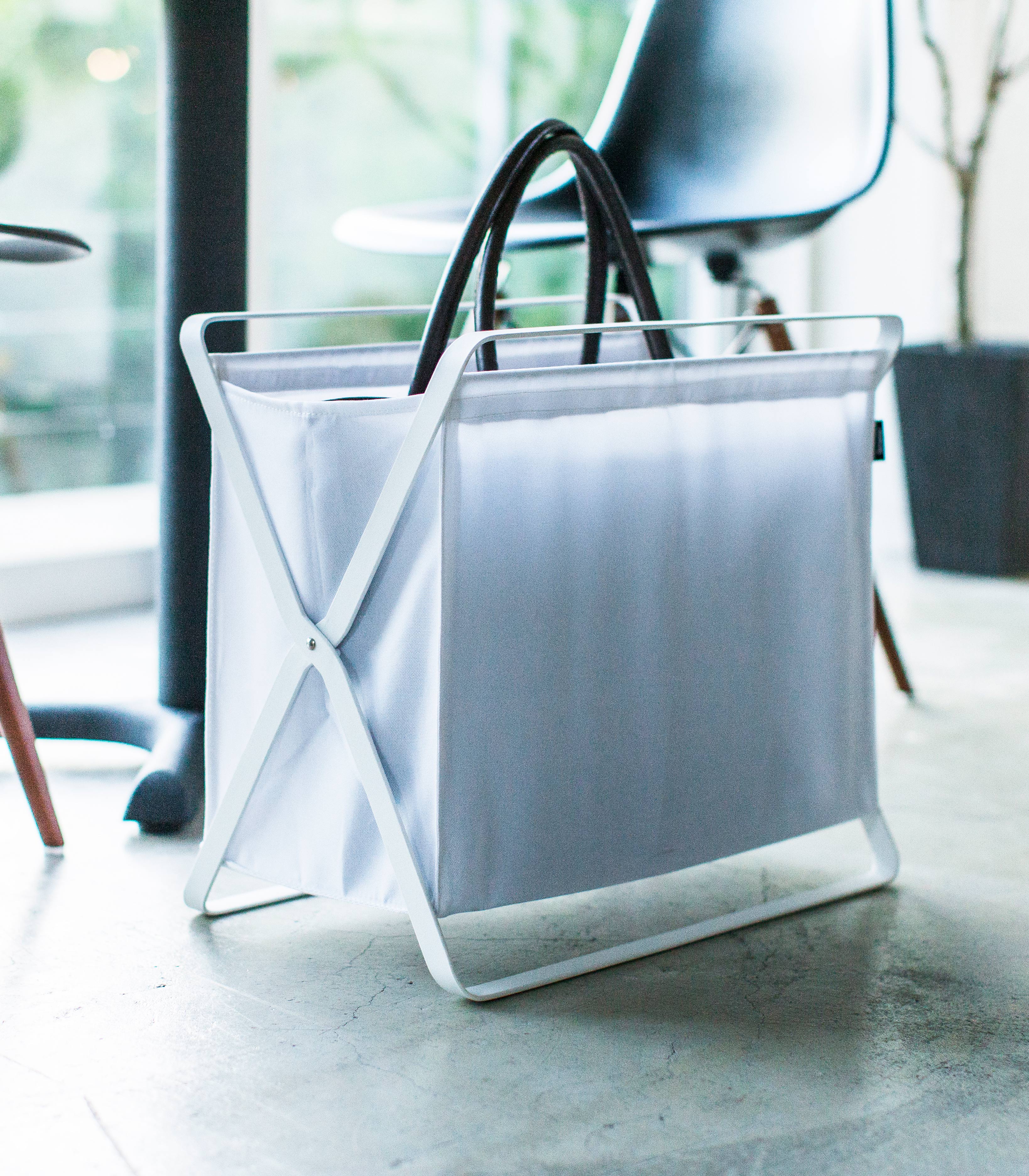 White magazine holder with black handles on a concrete floor