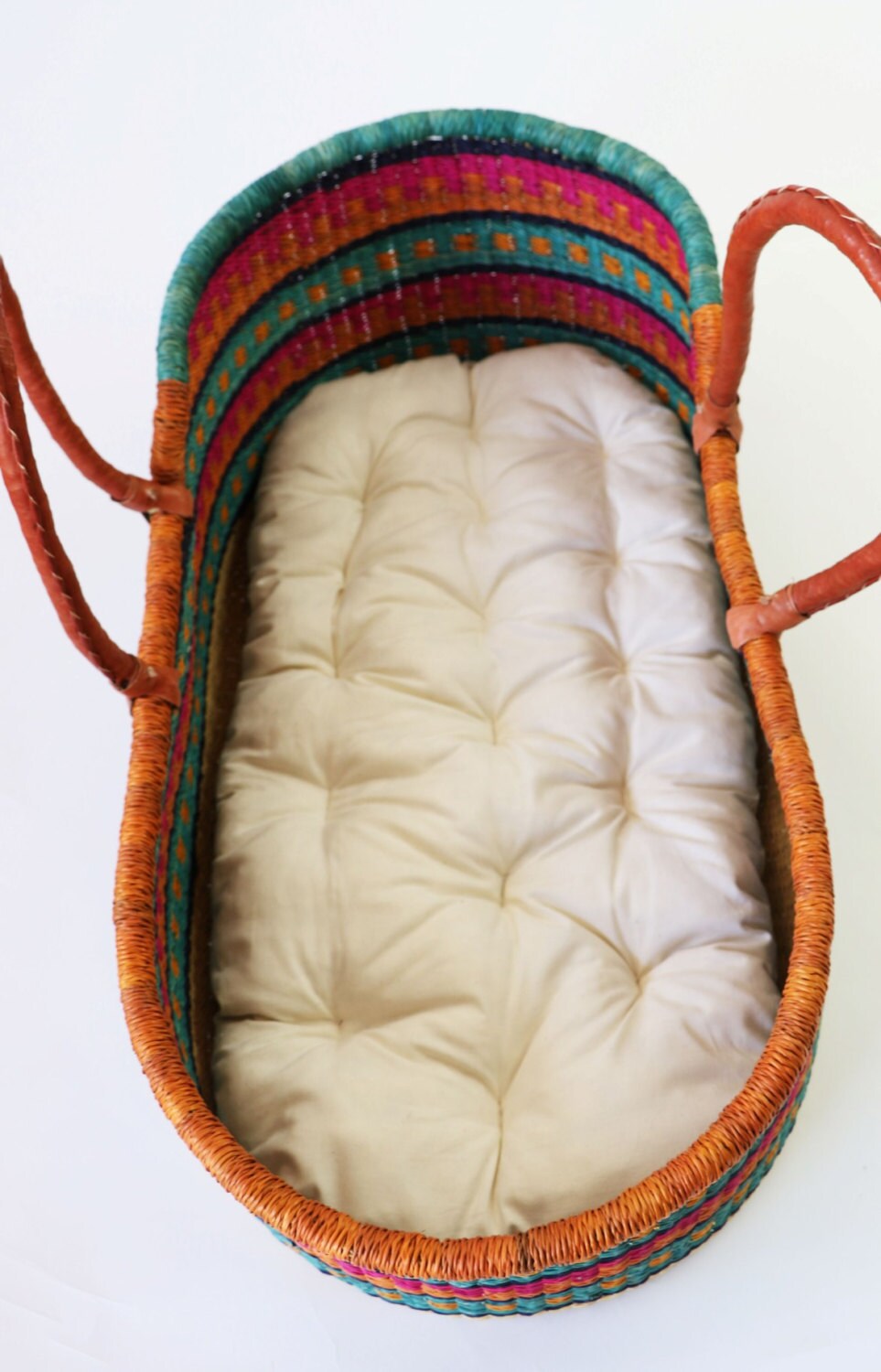 Woven baby crib with colorful top and white mattress on a white background