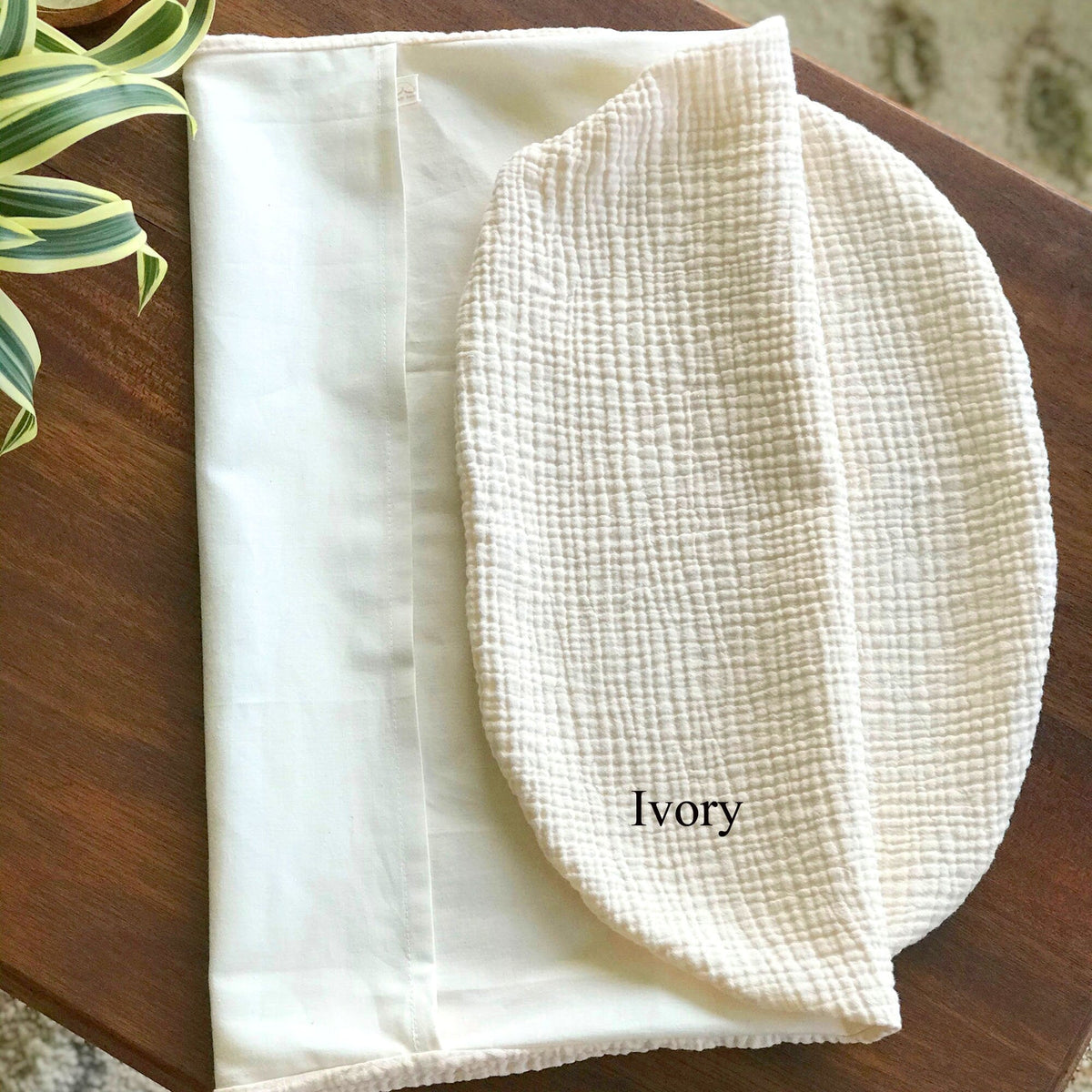 Ivory-colored fabric on a wooden surface with a plant in the corner.