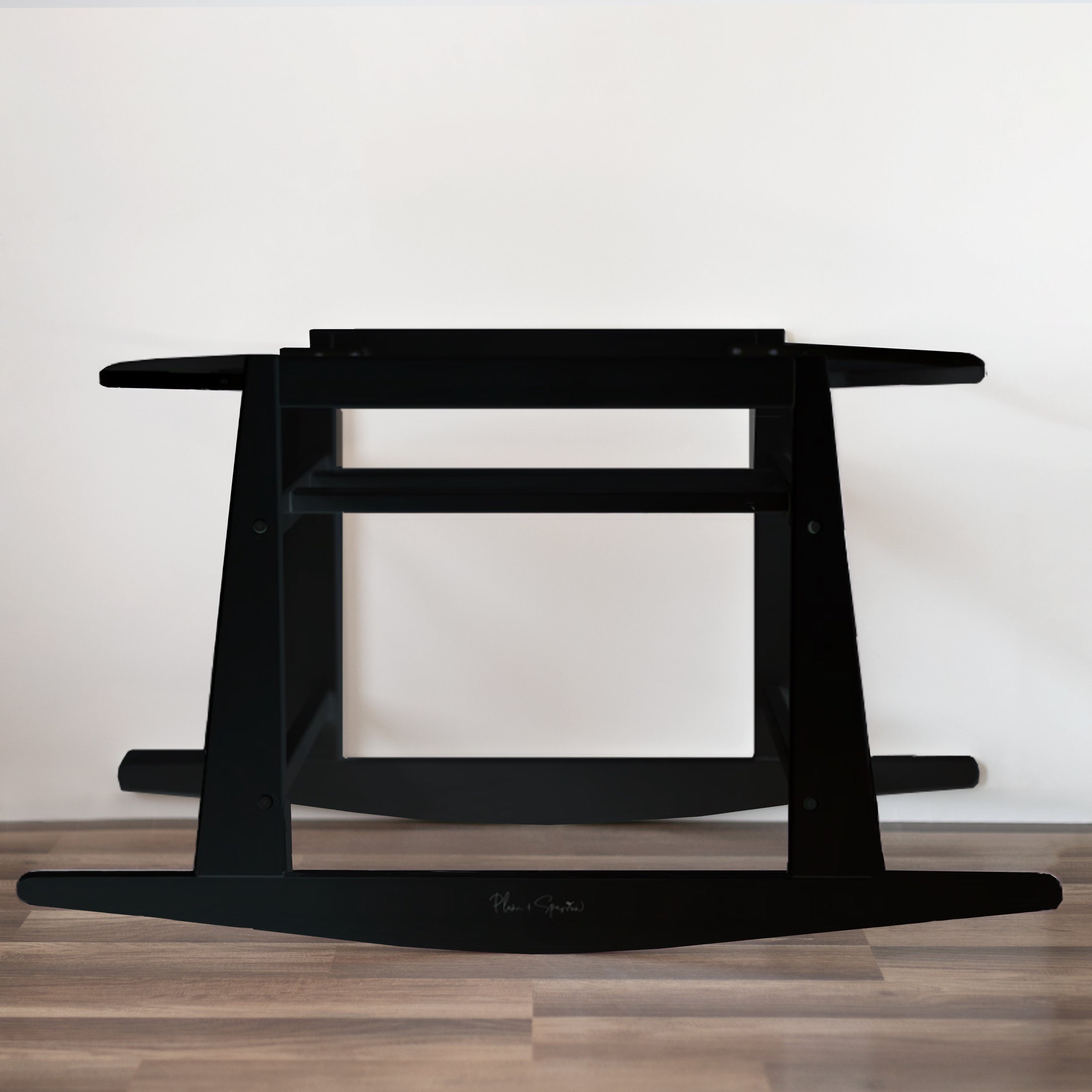 Black standing desk on a wooden floor with a white wall background