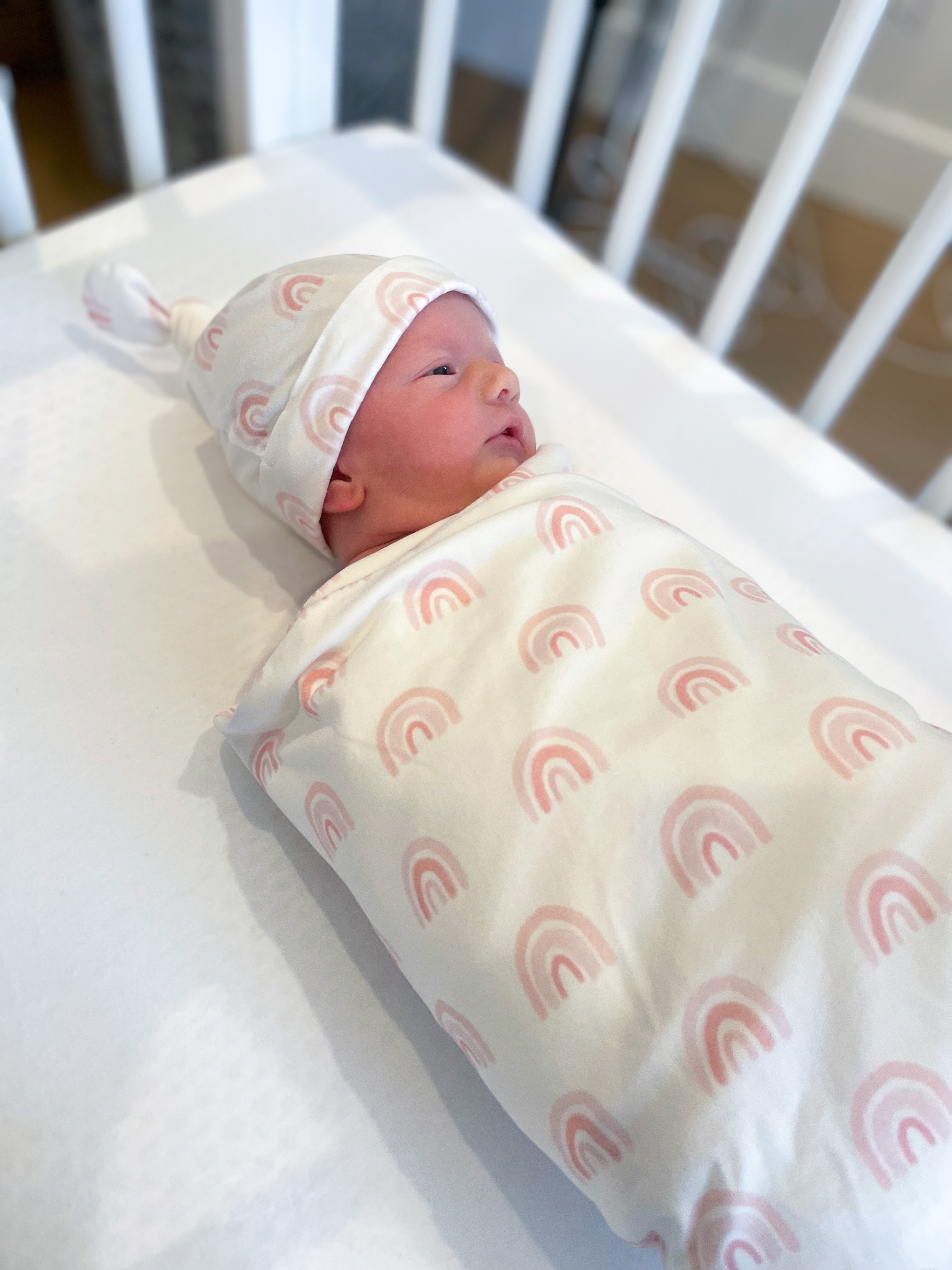 Newborn baby swaddled in a blanket with rainbow pattern in a crib.
