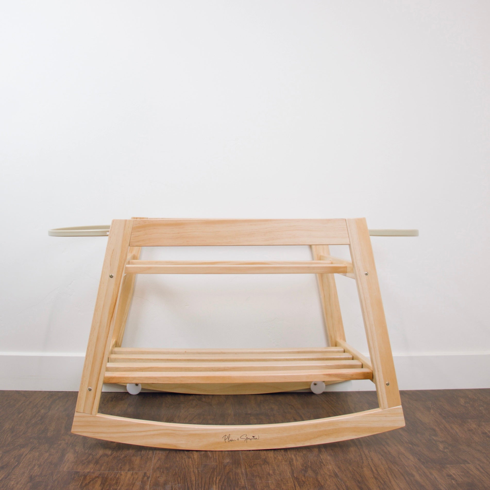 Wooden baby rocker on a wooden floor with a white wall background