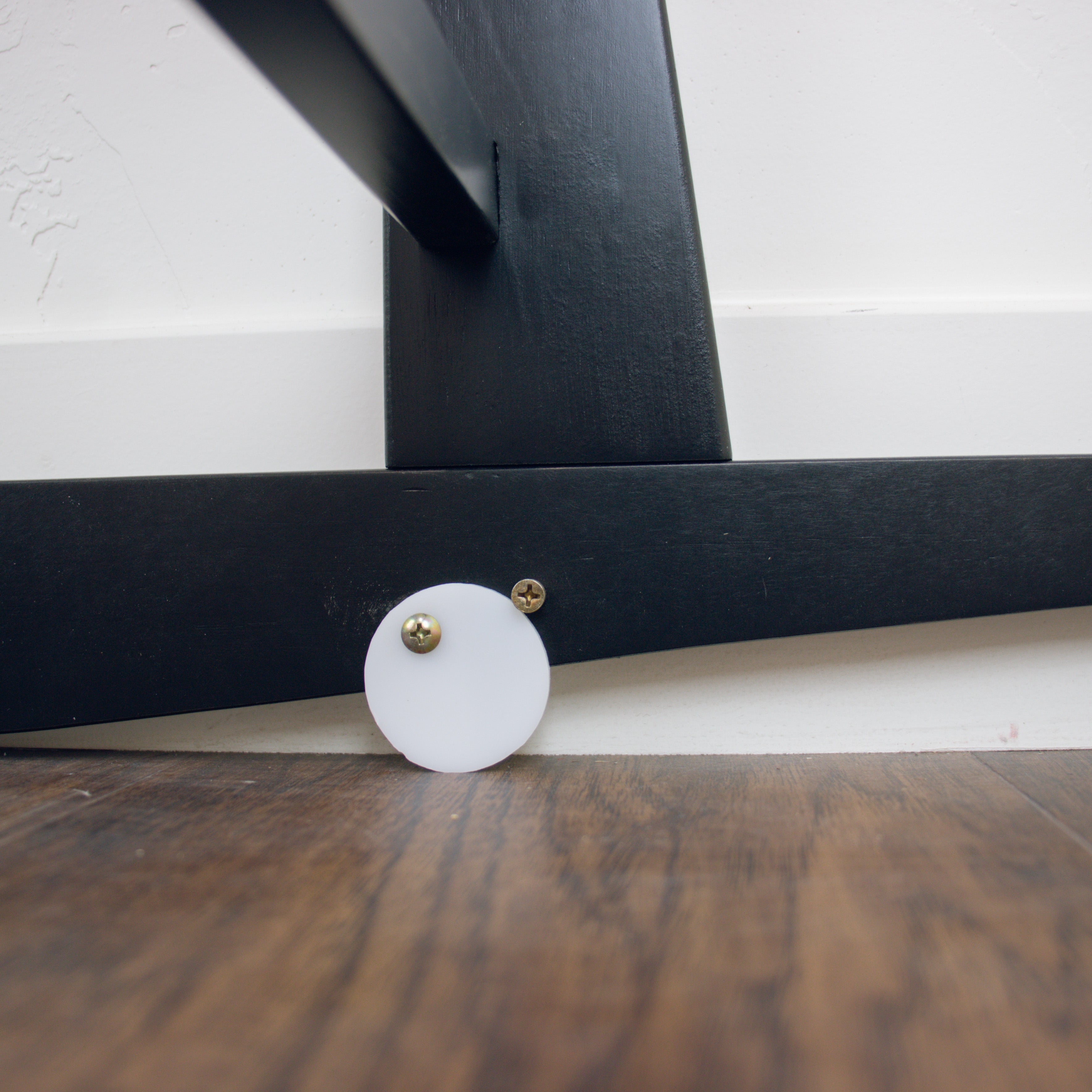 Close-up of a black metal frame with a white circular object on a wooden floor.