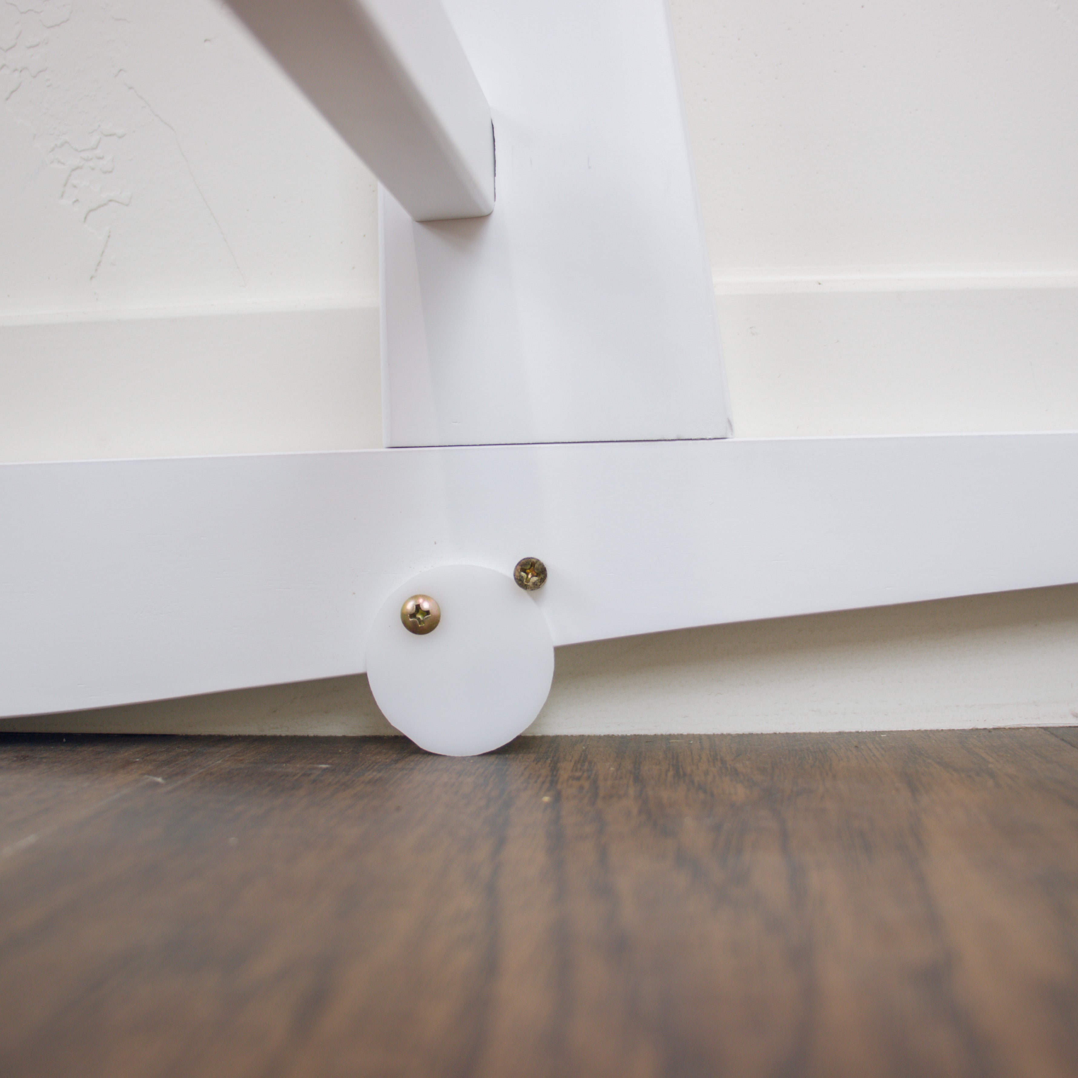Close-up of a white cabinet with a round leg on a wooden floor.