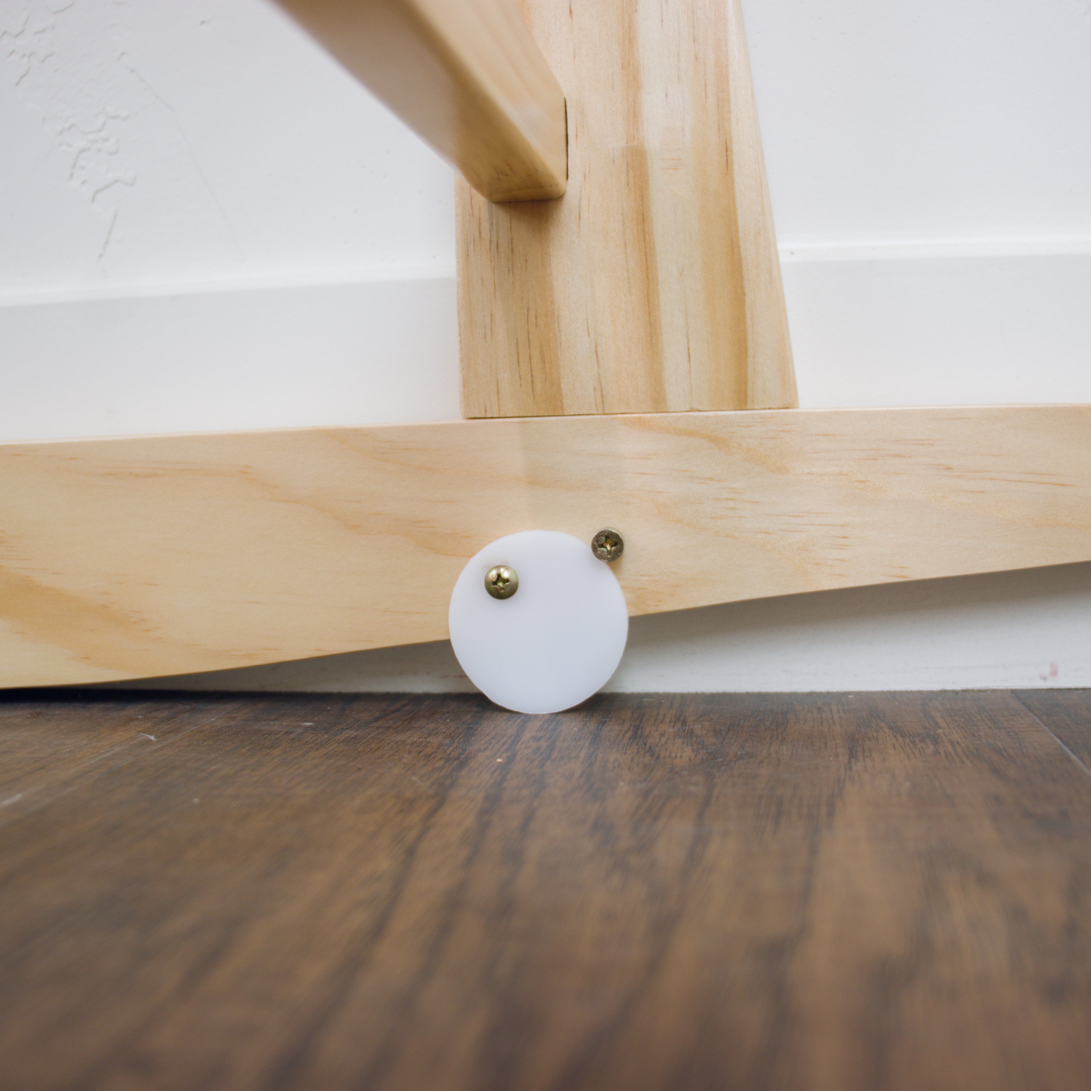 Wooden chair leg with a white circular foot pad on a wooden floor.