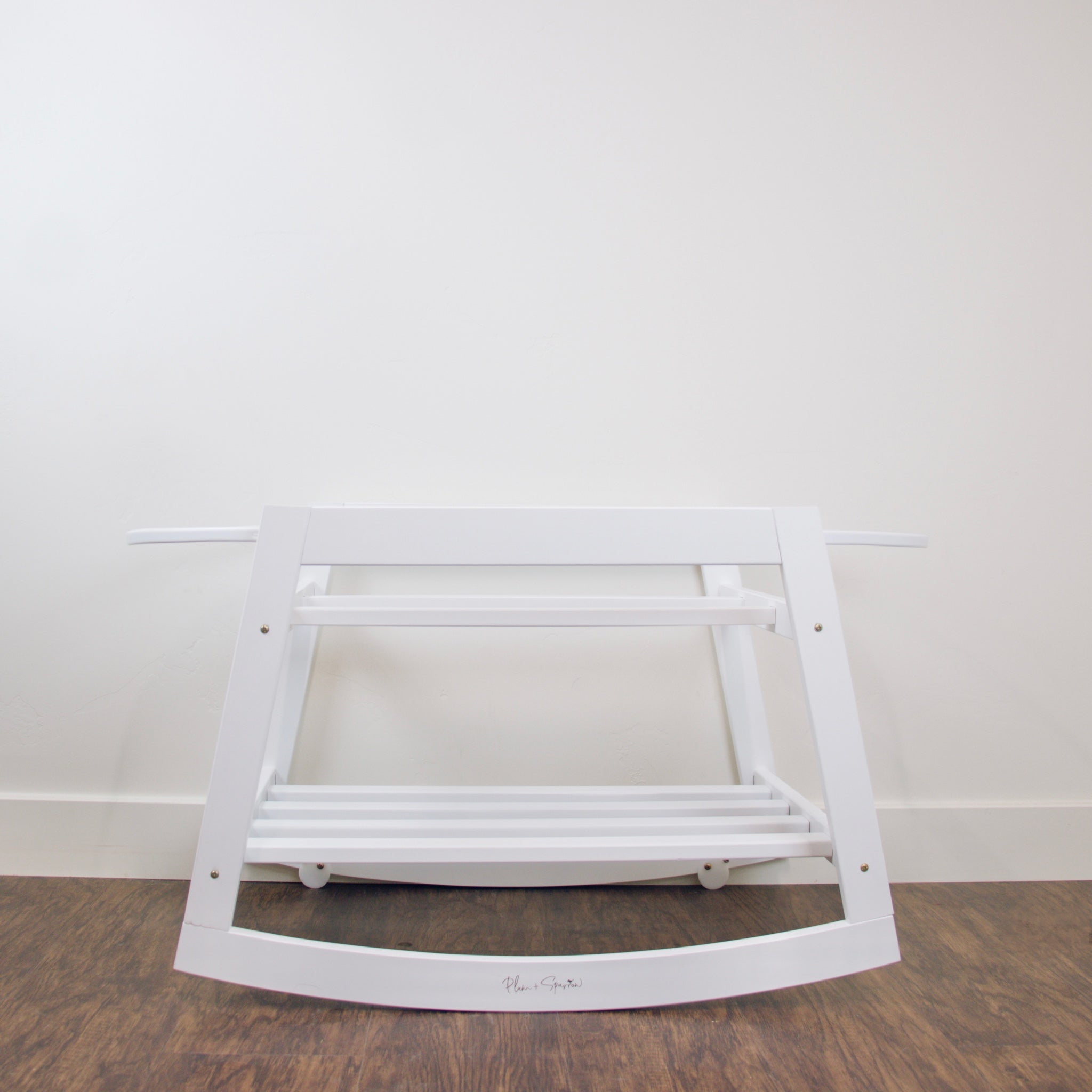 White rocking chair on a wooden floor with a plain white wall background